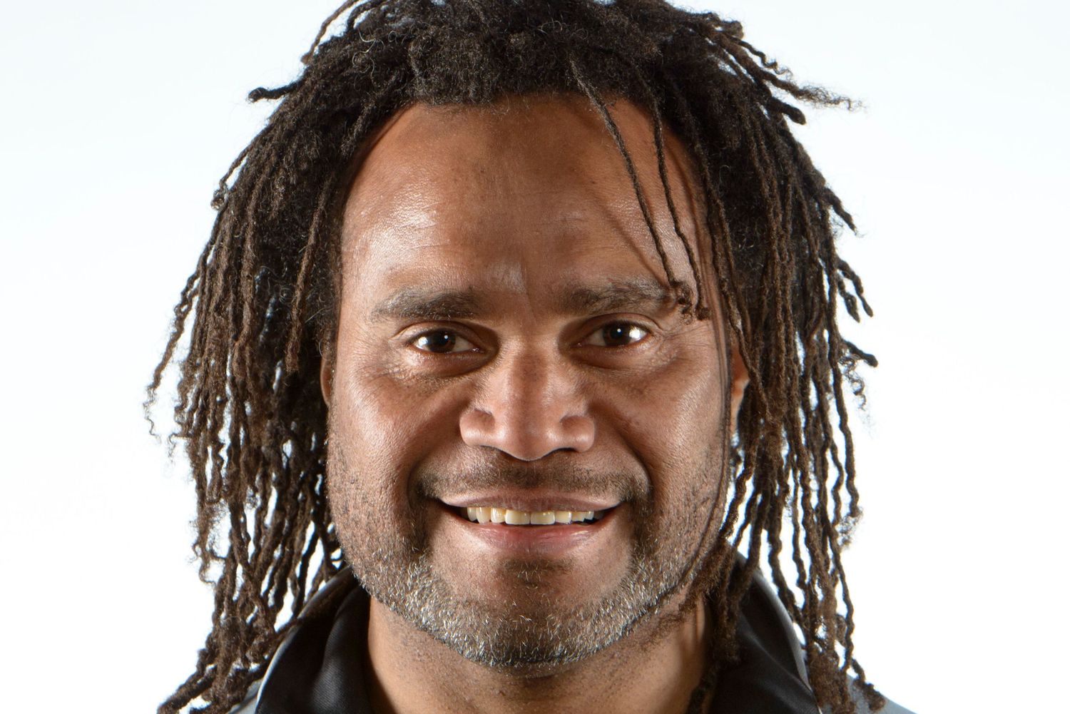Christian Karembeu with long dreadlocks and a gray beard smiles warmly at the camera.