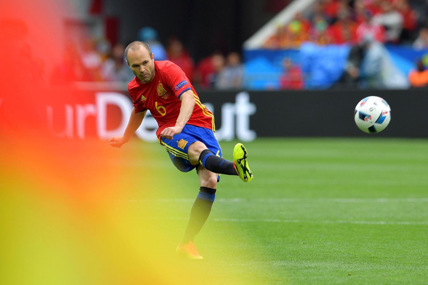 Soccer player in red Spain jersey kicks ball during a UEFA Euro championship match on green field.