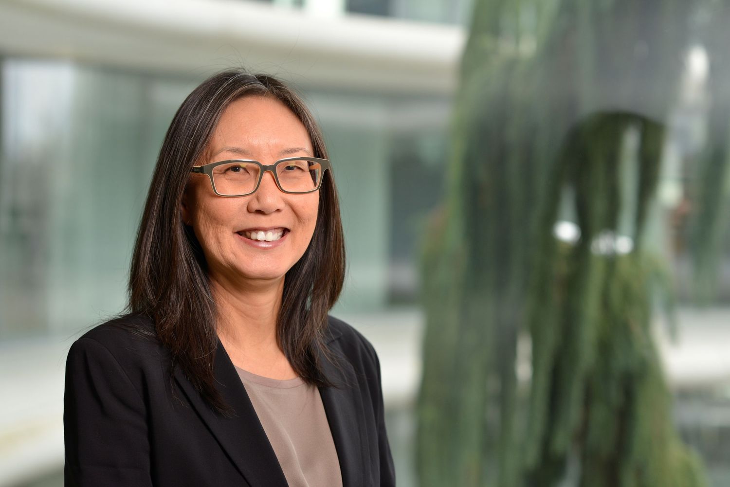 Woman in black blazer smiling in modern glass office building interior.
