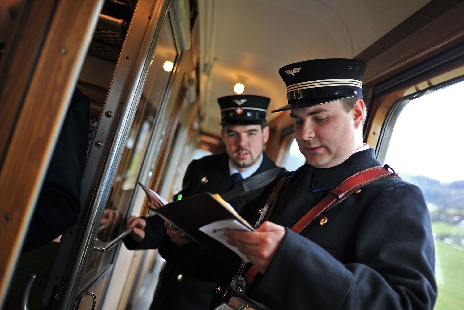 Two train conductors in uniform reviewing documents inside a passenger rail car.