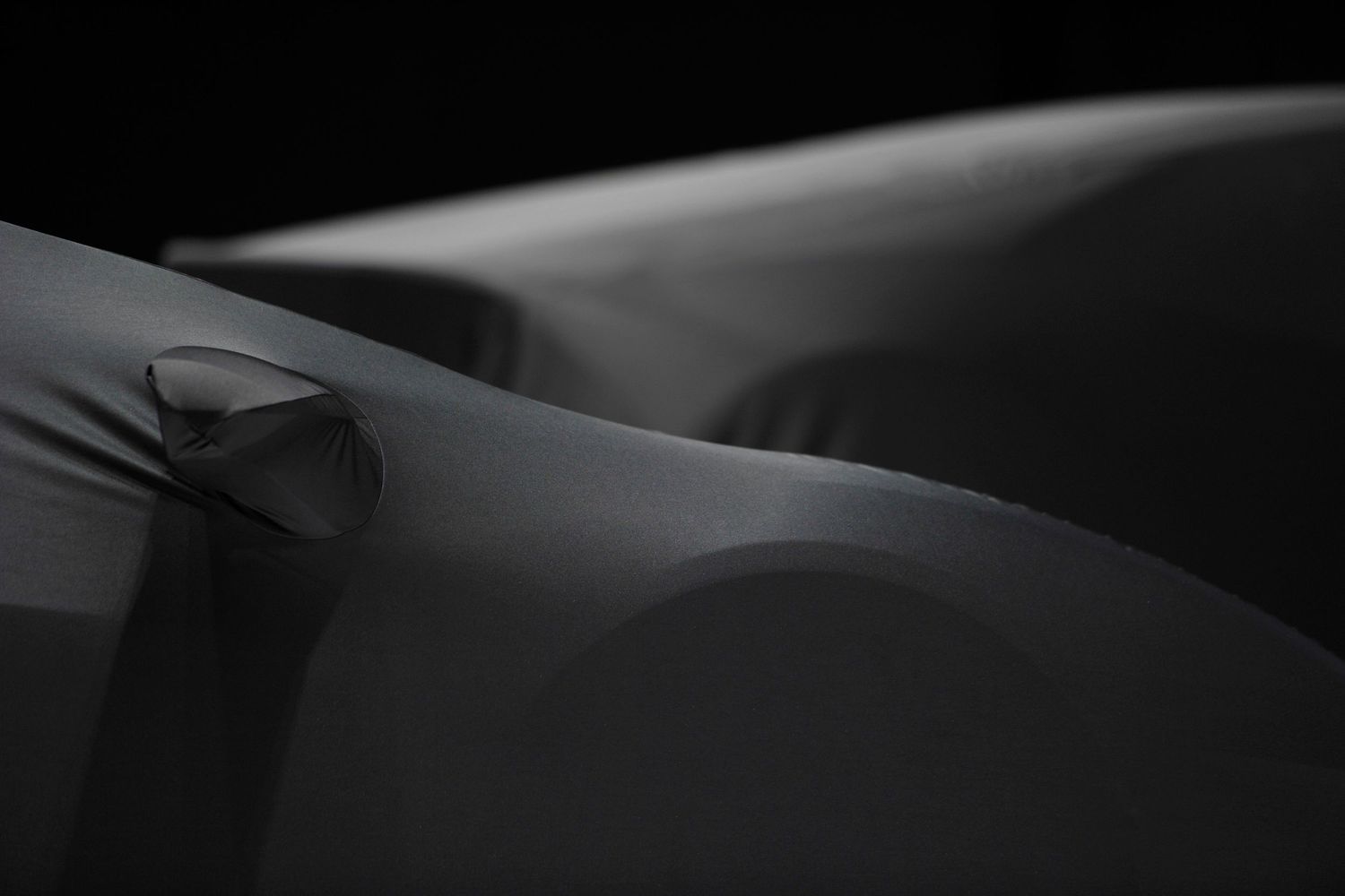 Abstract dark car artistic photograph of smooth curved surfaces with subtle light reflections on fabric.