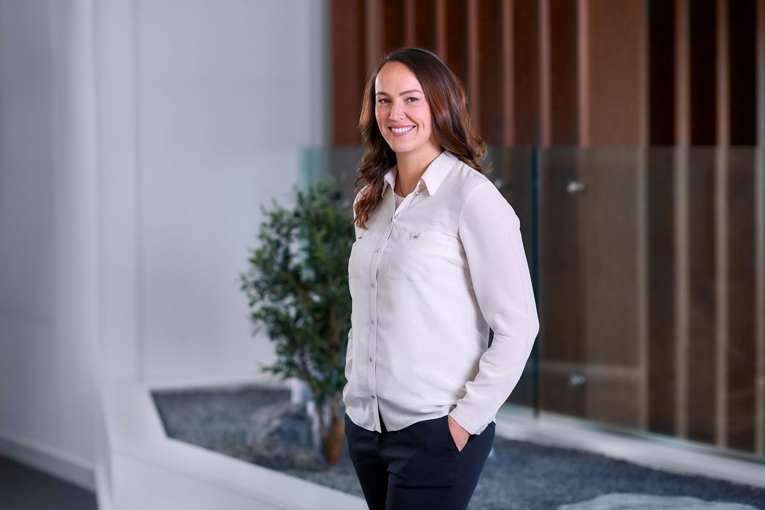 Smiling professional woman in white shirt standing in modern bright office corridor.