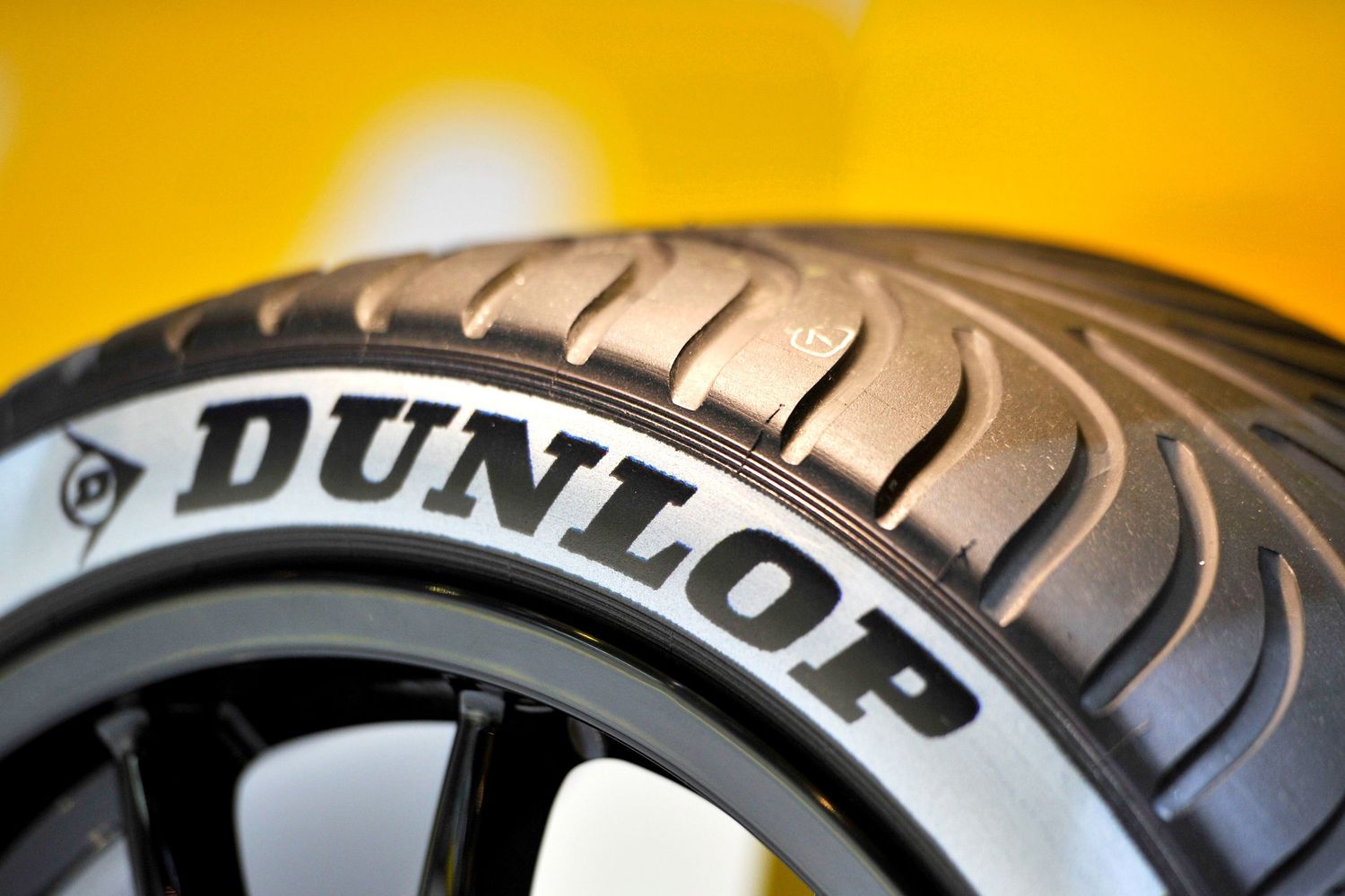 Dunlop branded performance tire mounted on a black alloy wheel on yellow background.