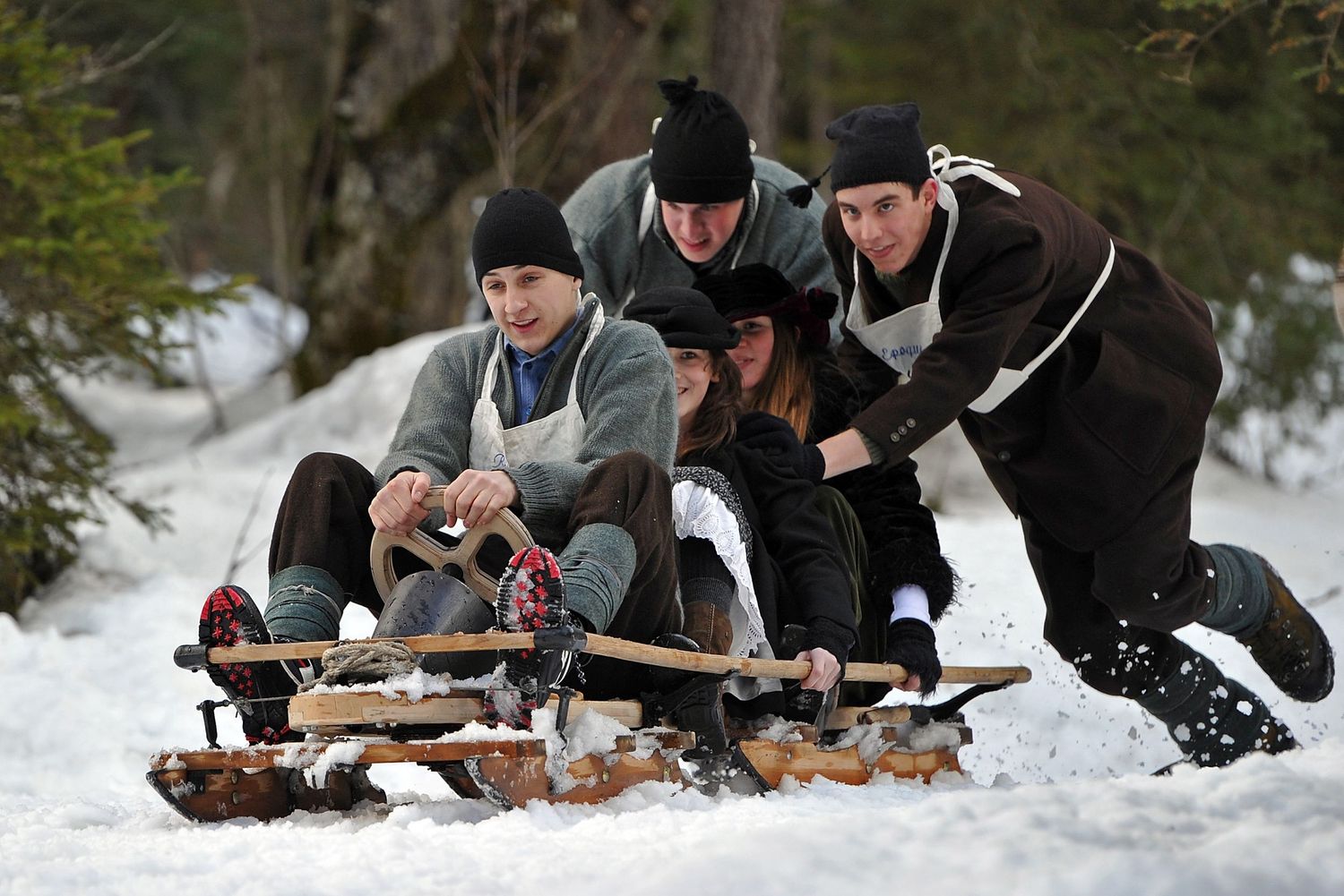 Group of young people laughing and sledding together on a snowy forest trail in winter.