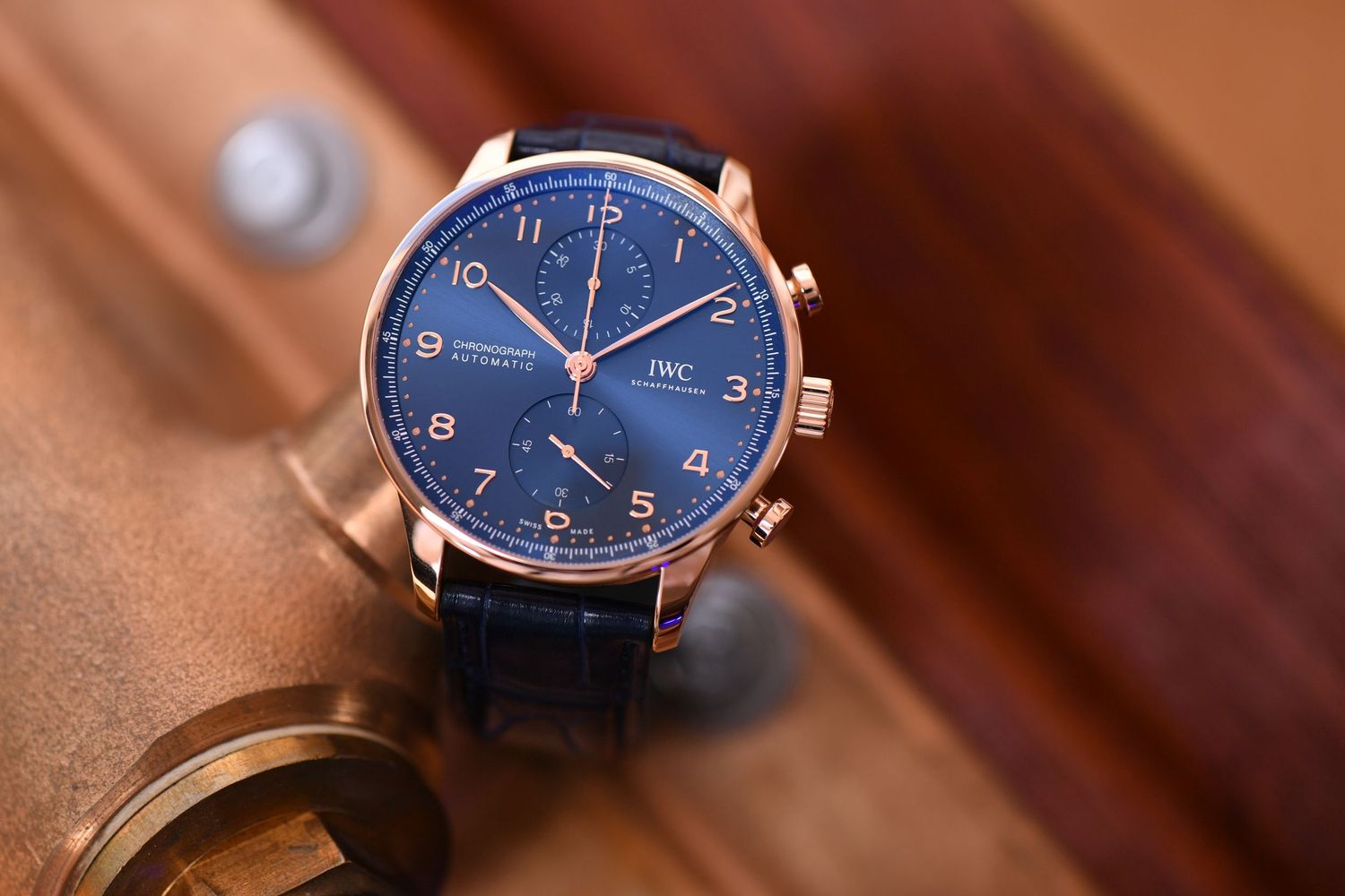IWC Portugieser chronograph watch with blue dial and rose gold case on wooden surface.