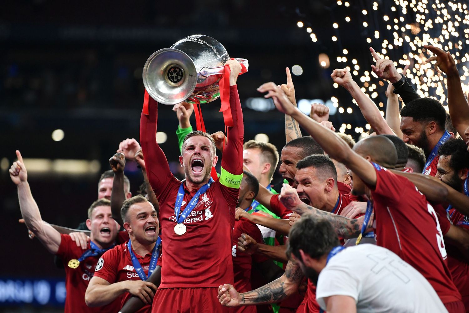Liverpool FC captain lifts UEFA Champions League trophy surrounded by celebrating teammates in red jerseys.