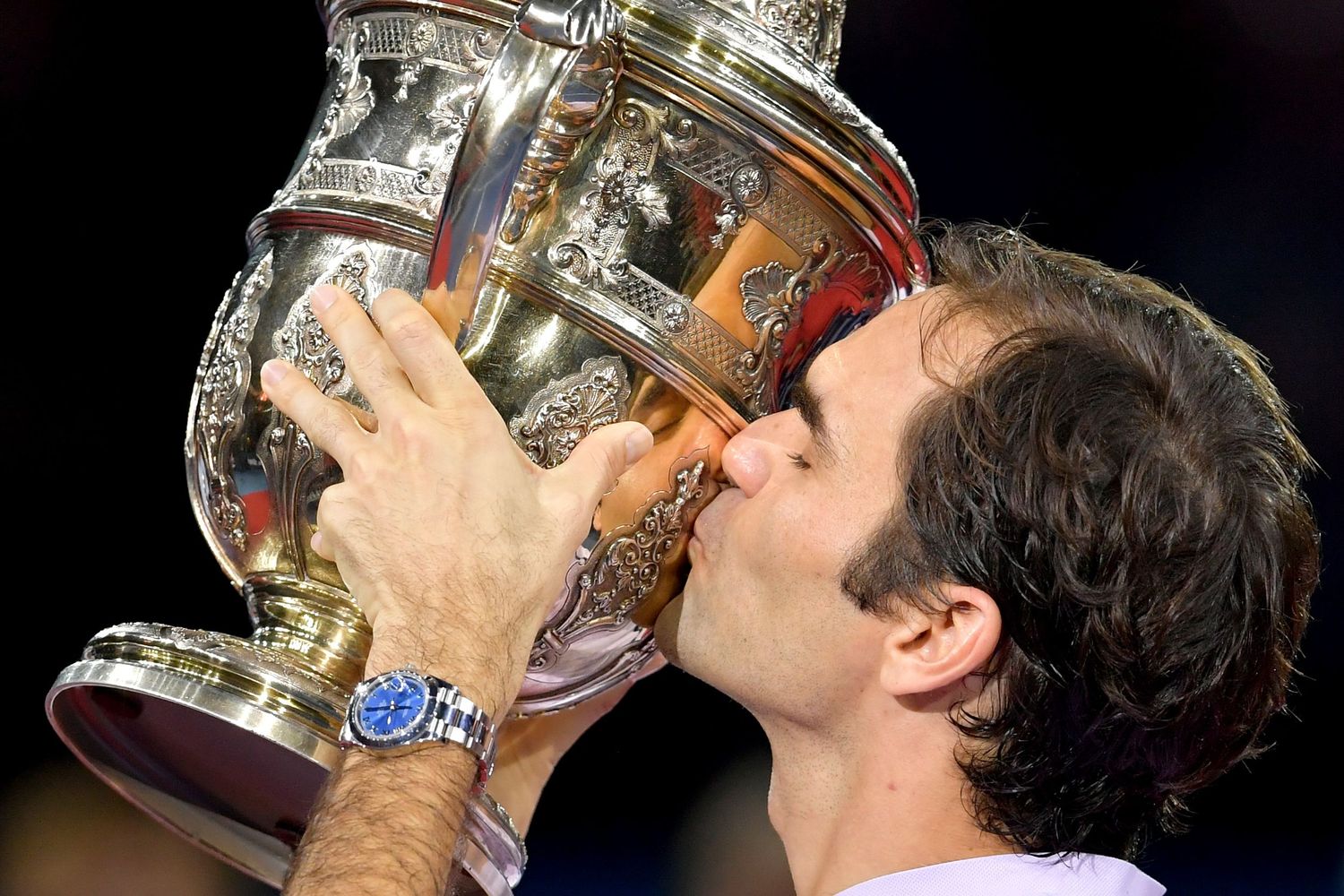 Tennis player kissing a large ornate silver trophy cup after winning a championship match.