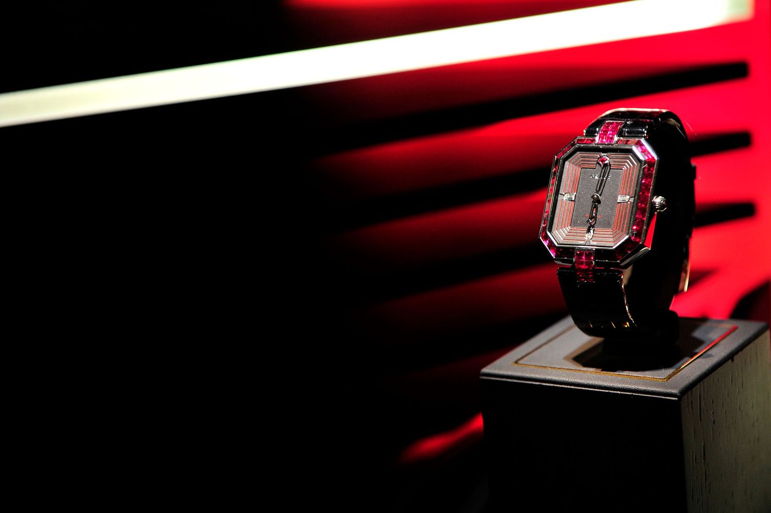 Luxury square-faced wristwatch displayed on a stand with dramatic red lighting background.