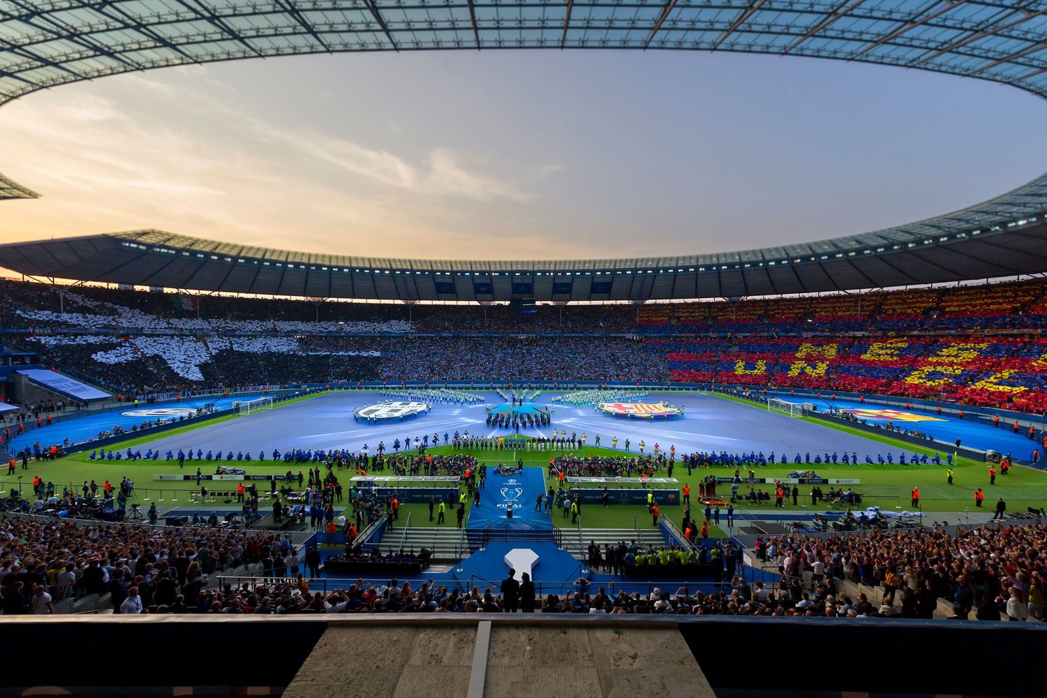 Panoramic view of a packed UEFA Champions League stadium at dusk with colorful fan displays and teams lined up.