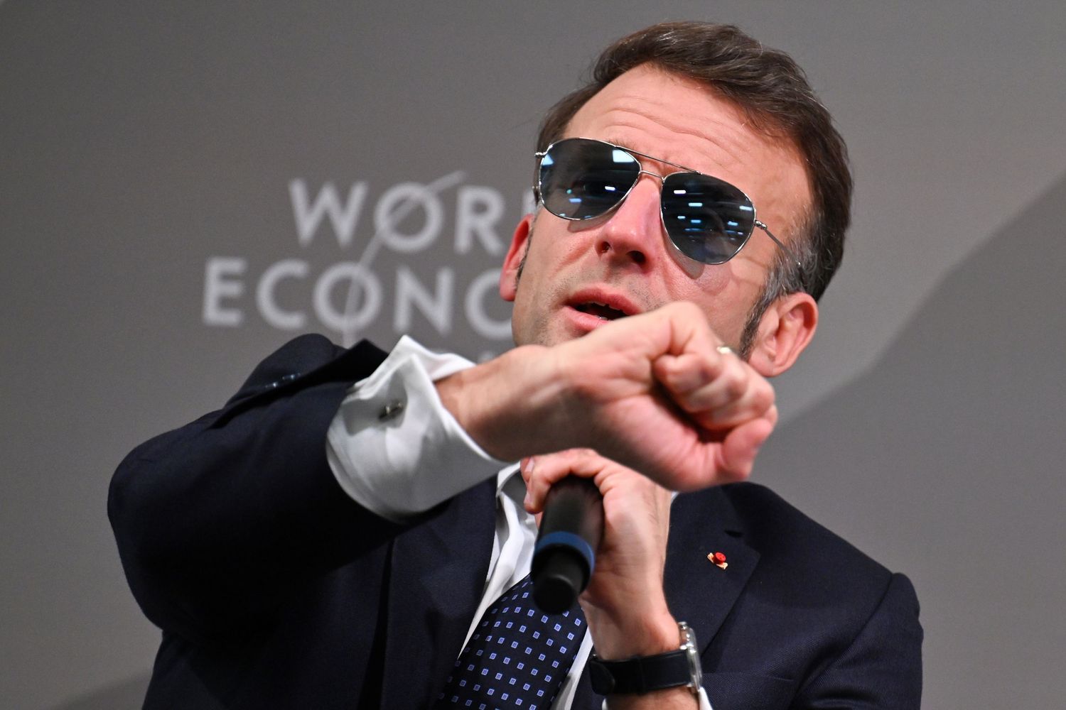 Man in sunglasses and suit gestures at World Economic Forum panel discussion event.