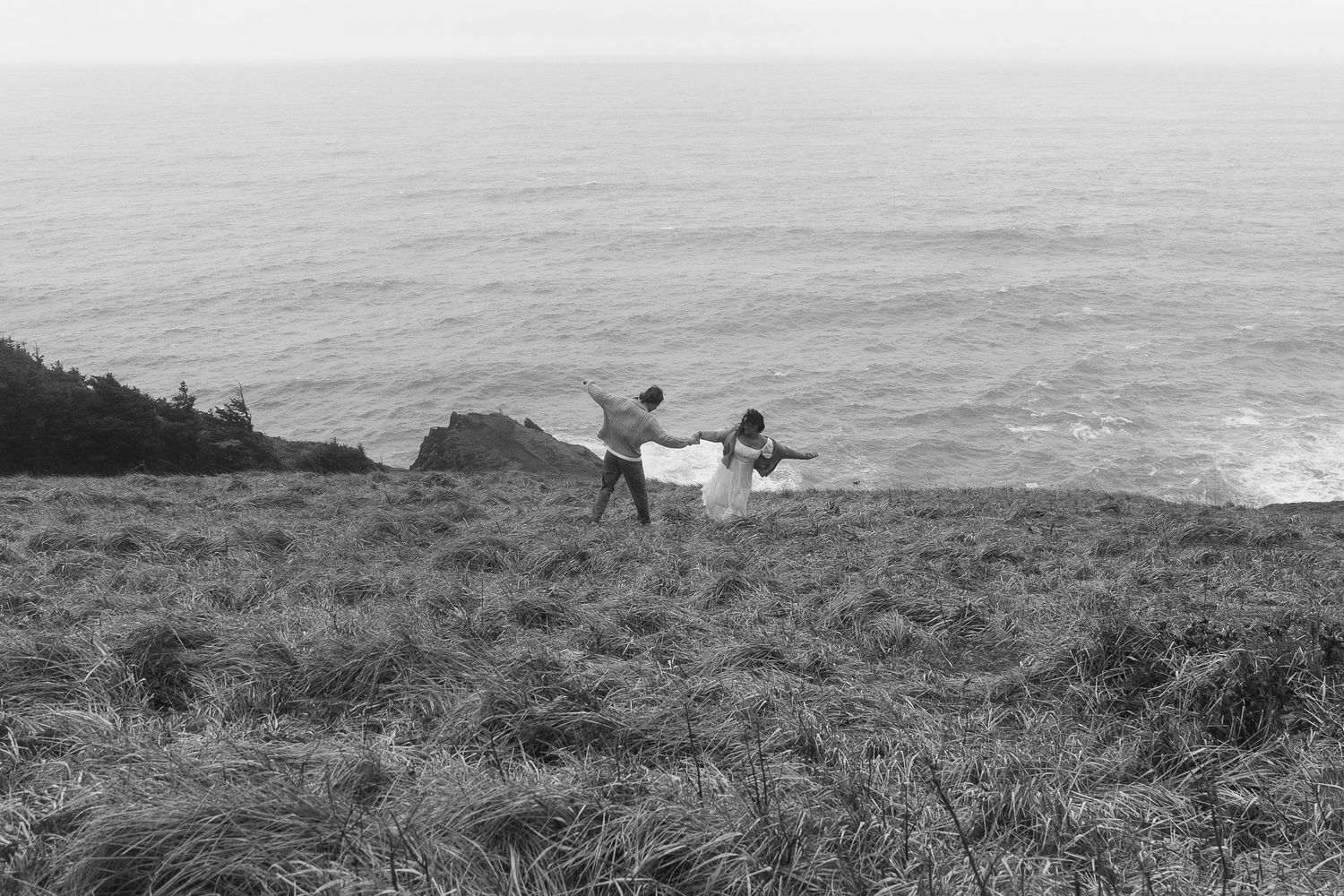 Two figures stand on a cliff overlooking the ocean in black and white.