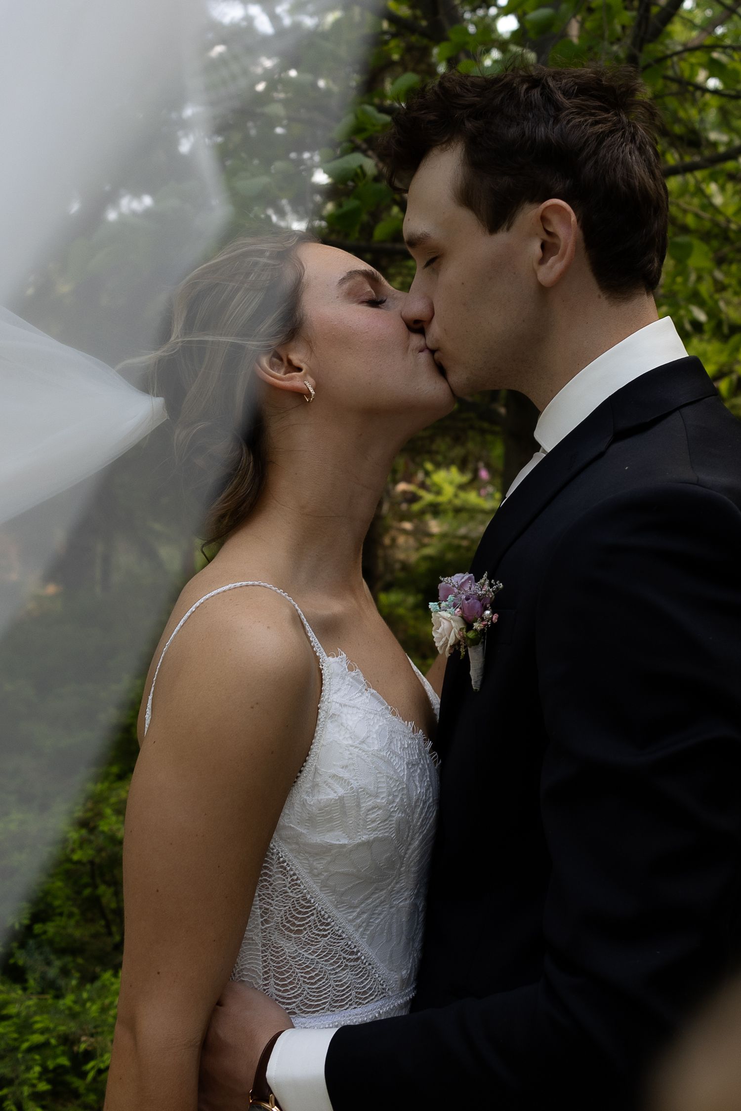A romantic wedding kiss moment captured in a garden setting with soft natural lighting.