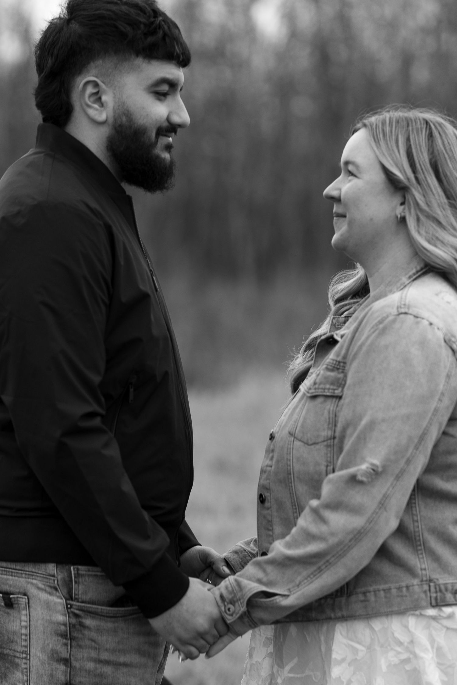 Black and white photo of a couple holding hands and gazing at each other outdoors.