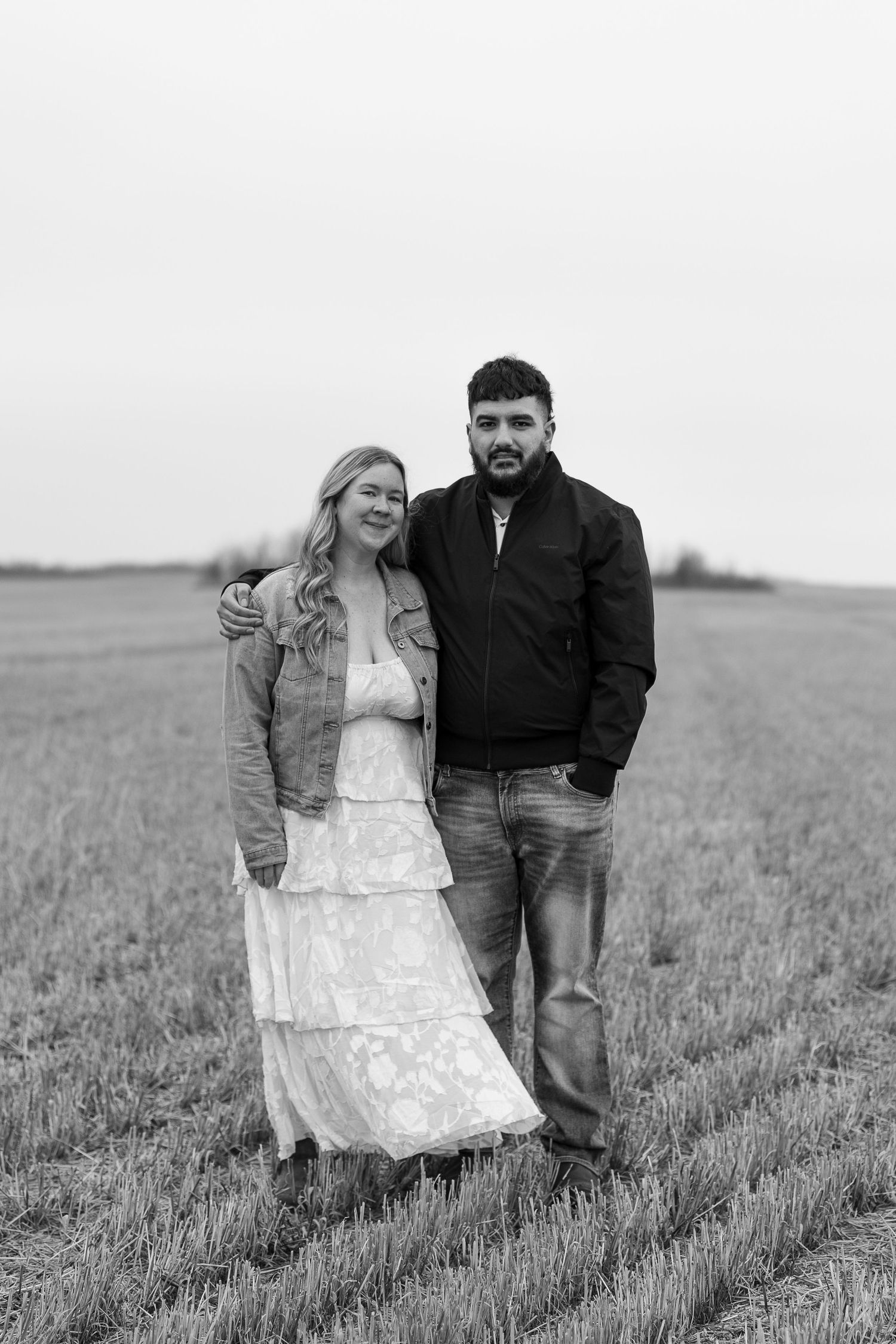 Couple stands together in a field wearing casual attire in black and white.
