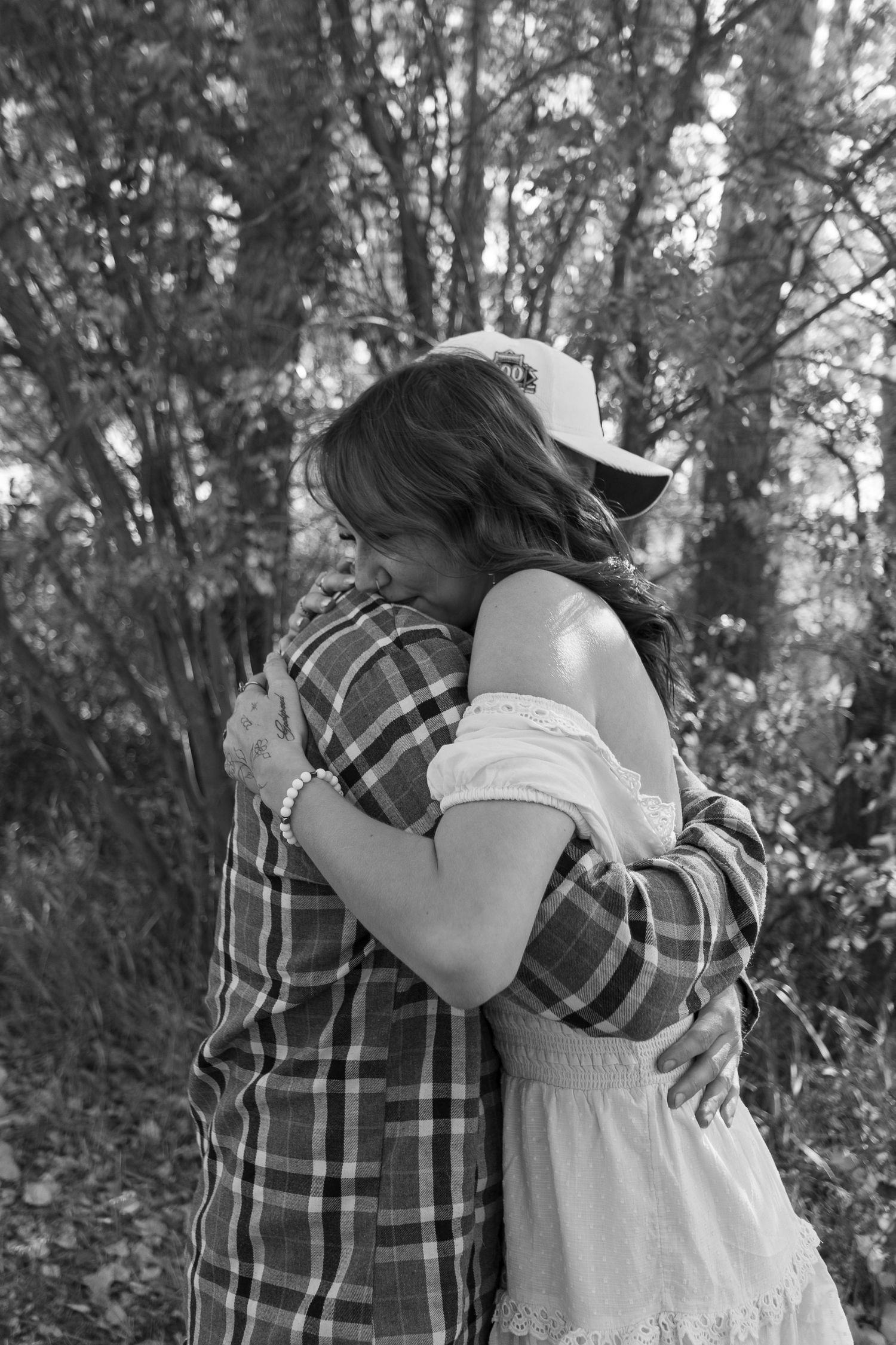 A tender embrace captured in black and white against a backdrop of trees.