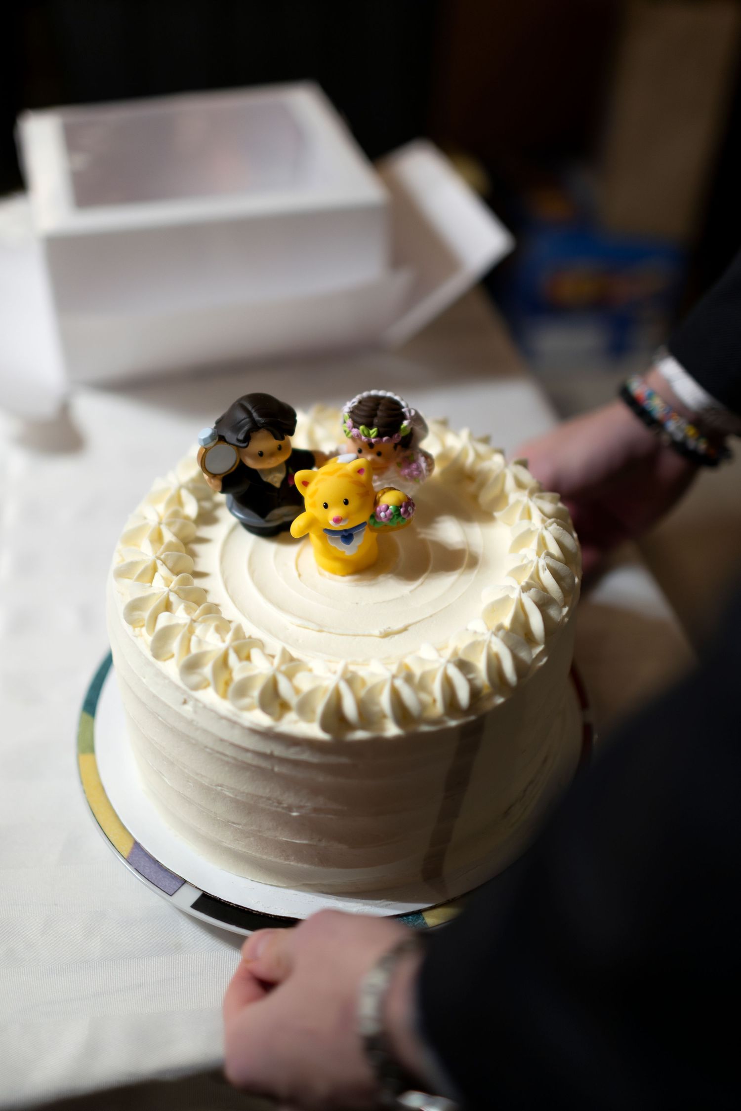 White wedding cake with bride and groom figurine toppers on a silver cake board.