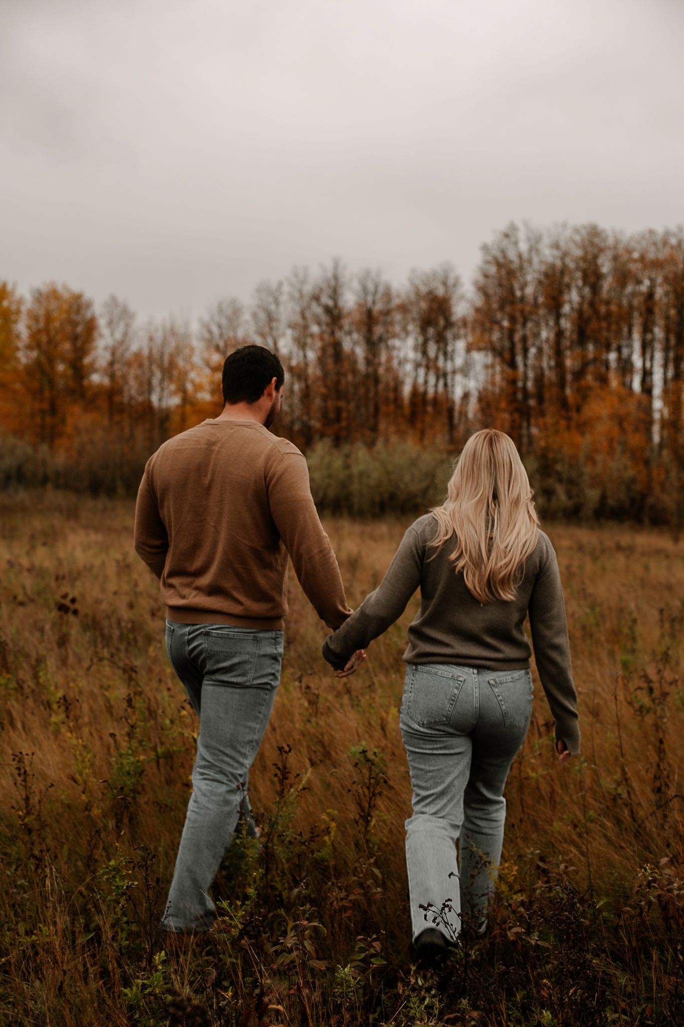People stroll through autumn field with orange trees on horizon.