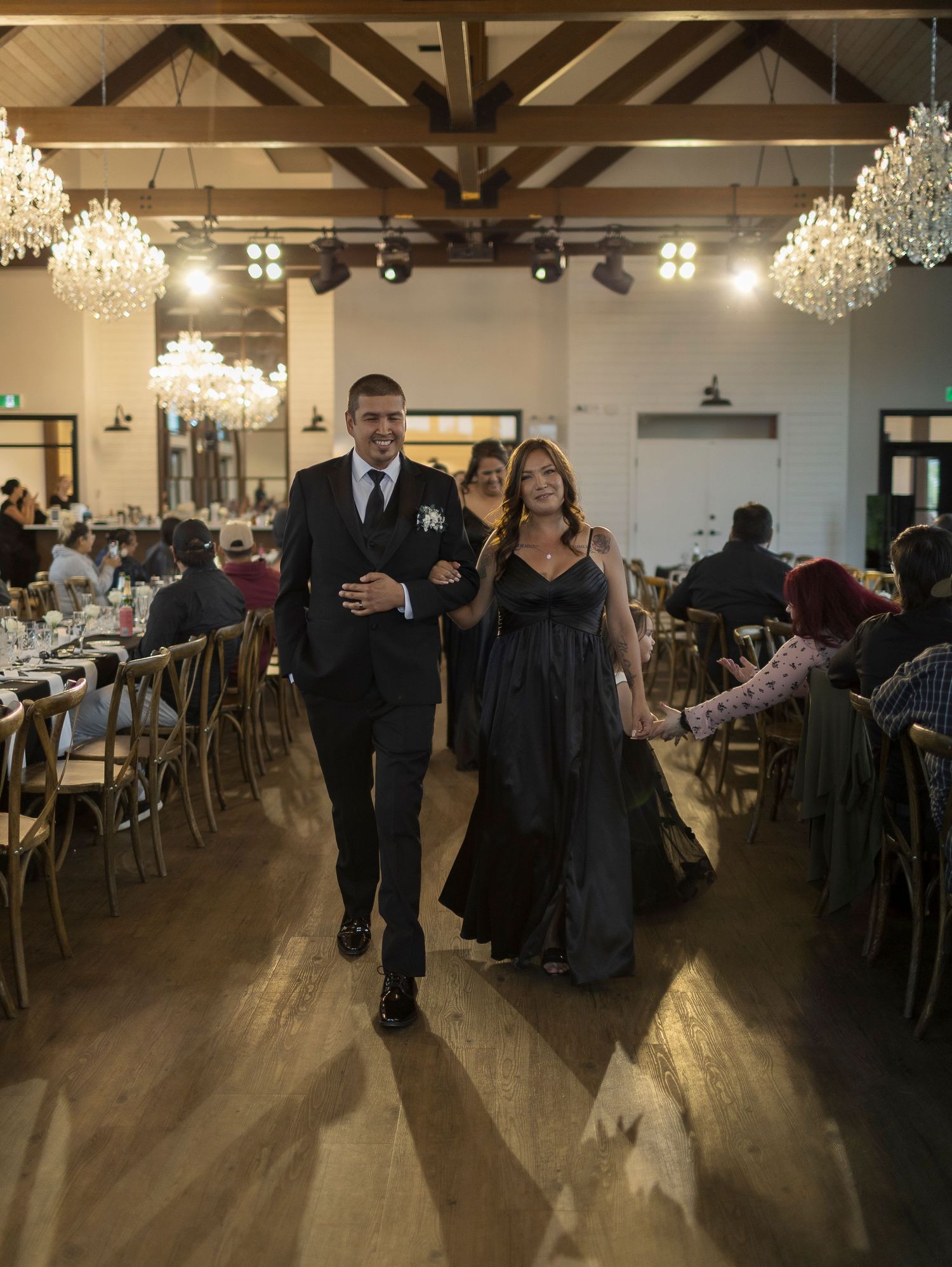 A spacious wedding reception venue with wooden beams, chandeliers, and elegant table settings.