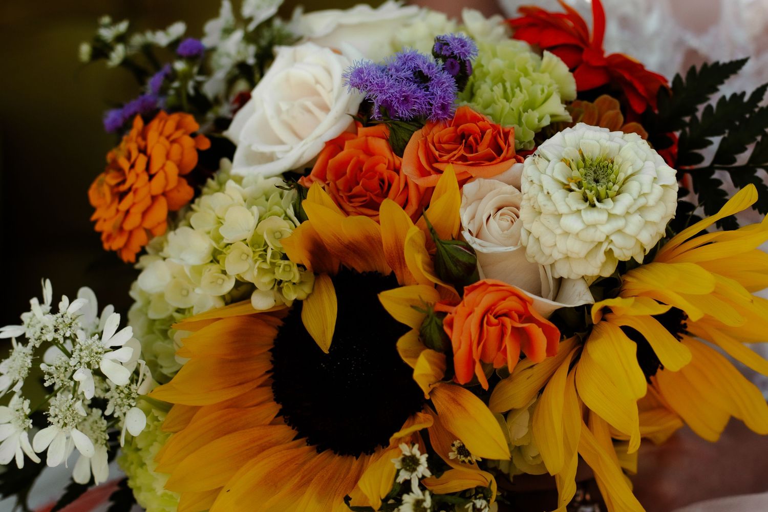 Vibrant wedding centerpiece with sunflowers, orange blooms, and purple accents.