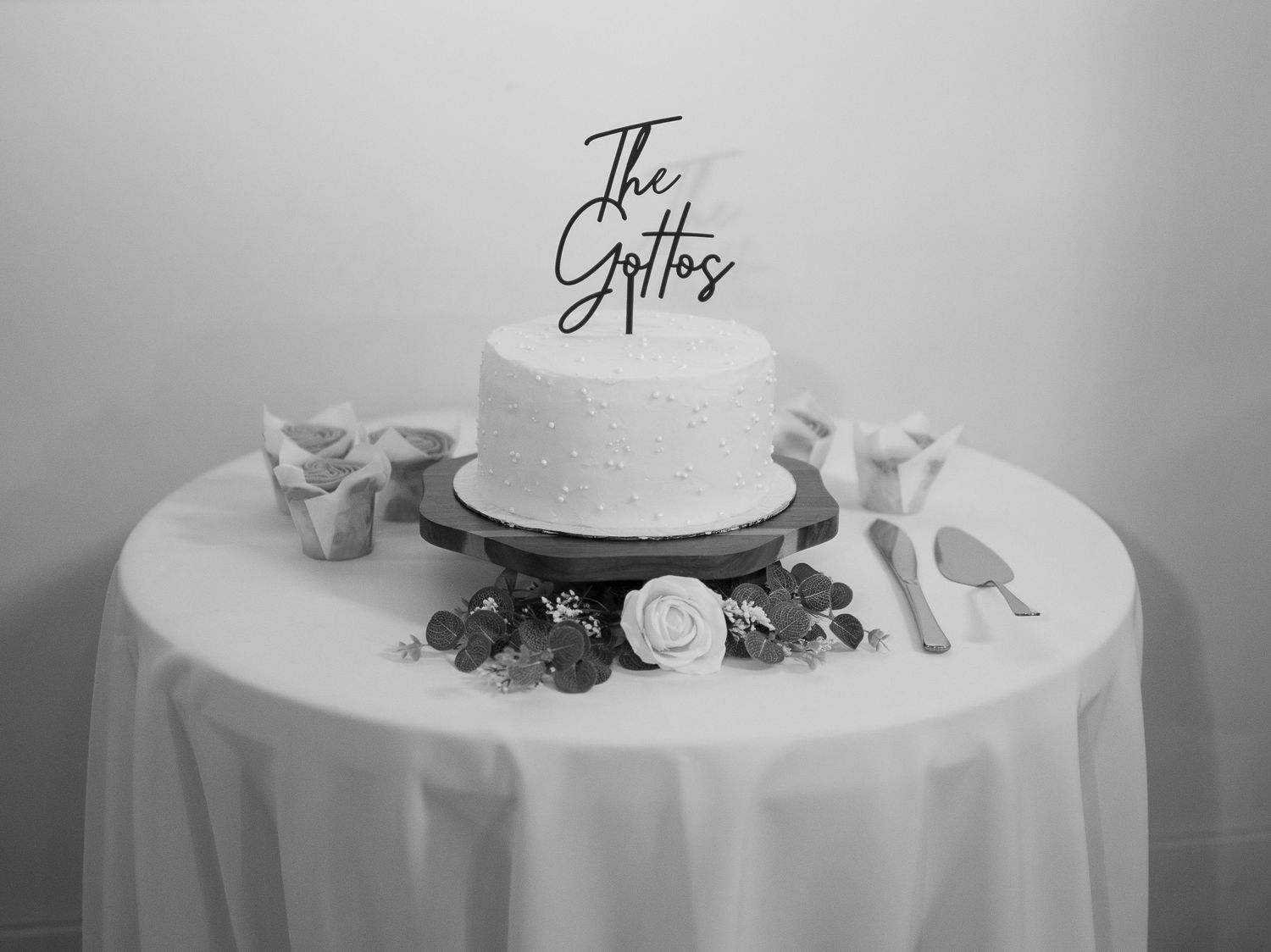An elegant white wedding cake displayed on a round table with delicate floral decorations at the Avenue Room in Saskatoon, Saskatchewan.