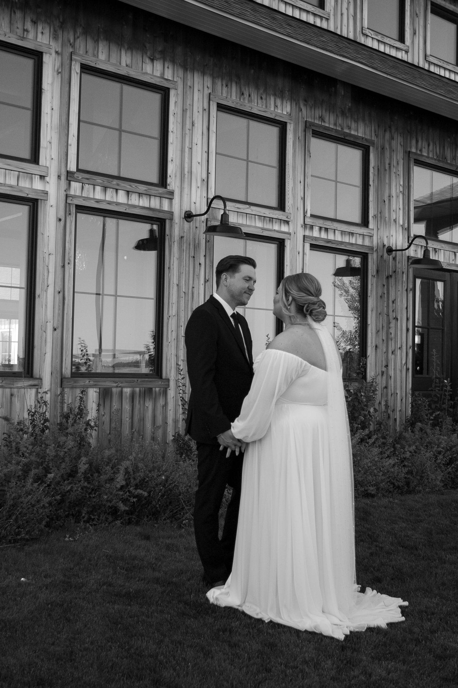 Black and white photo of a couple in formal attire outside a building at the Barn at Wind's Edge in Saskatoon, Saskatchewan.