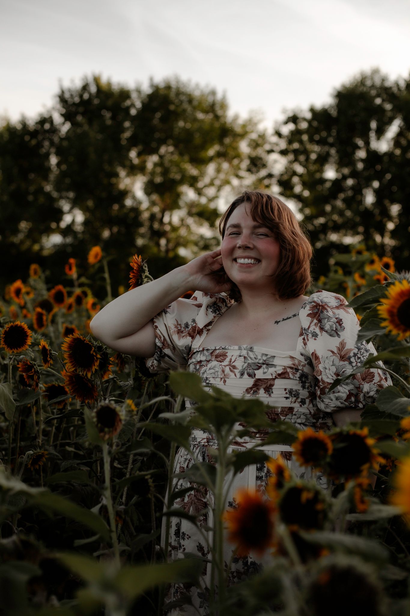 Person in floral dress poses joyfully among blooming sunflowers.