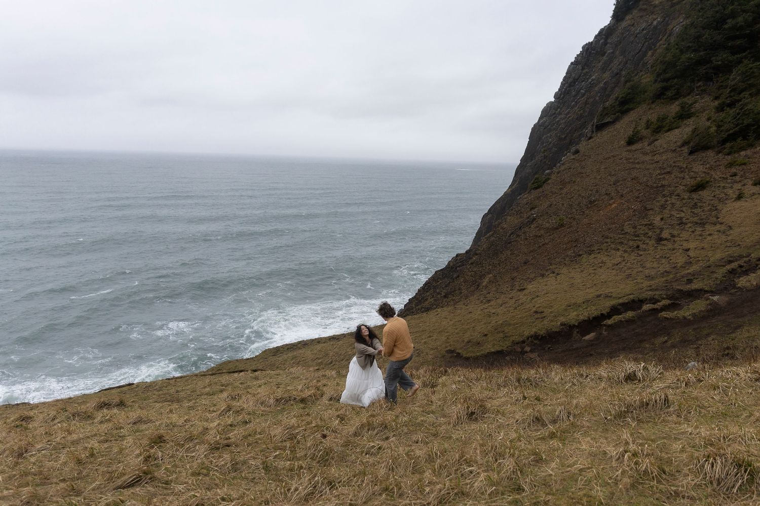 Distant view of a couple sitting on a dramatic coastal cliff overlooking the ocean.