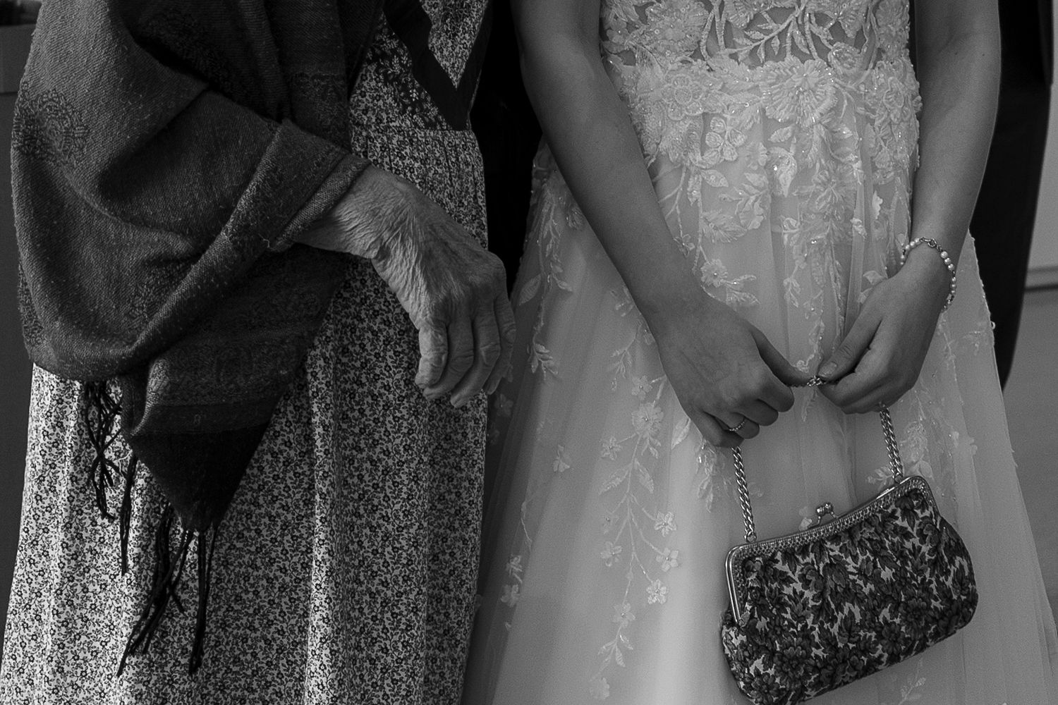 Black and white photo of elderly woman and bride standing together, bride holding decorative clutch purse.