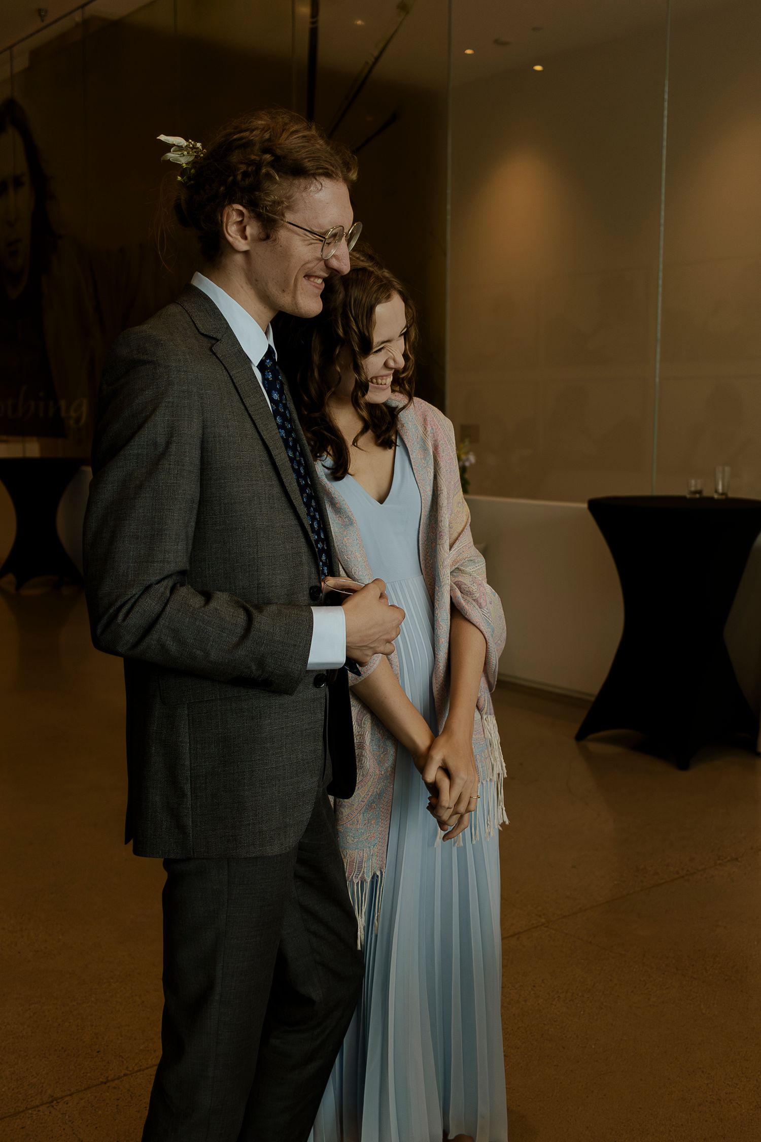 Couple in formal attire smiling and holding hands at an elegant indoor event venue.