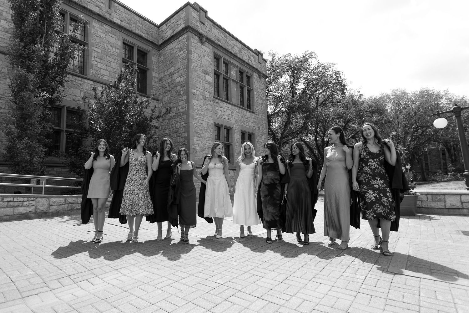 Black and white photo of a bride and bridesmaids posing outdoors in front of a stone building on a sunny day.