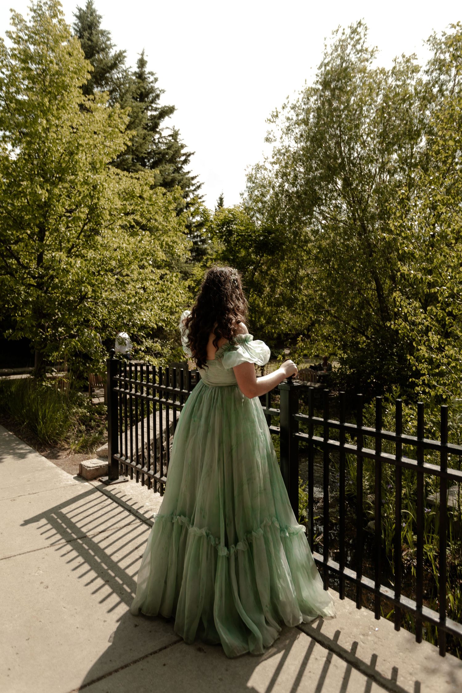 Bridesmaids in elegant sage green dresses pose along a railing outdoors.