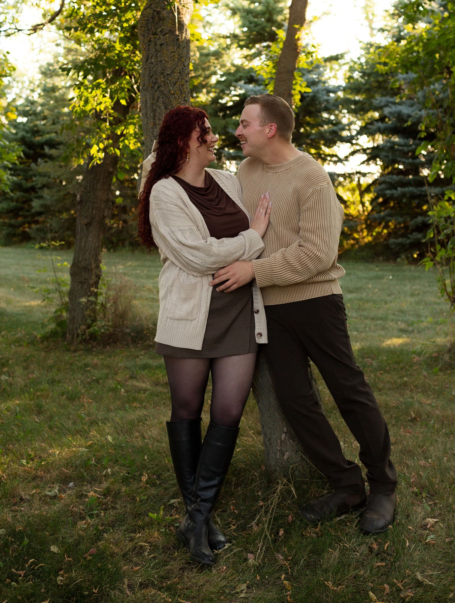 Couple embraces against a tree in autumn sunlight.