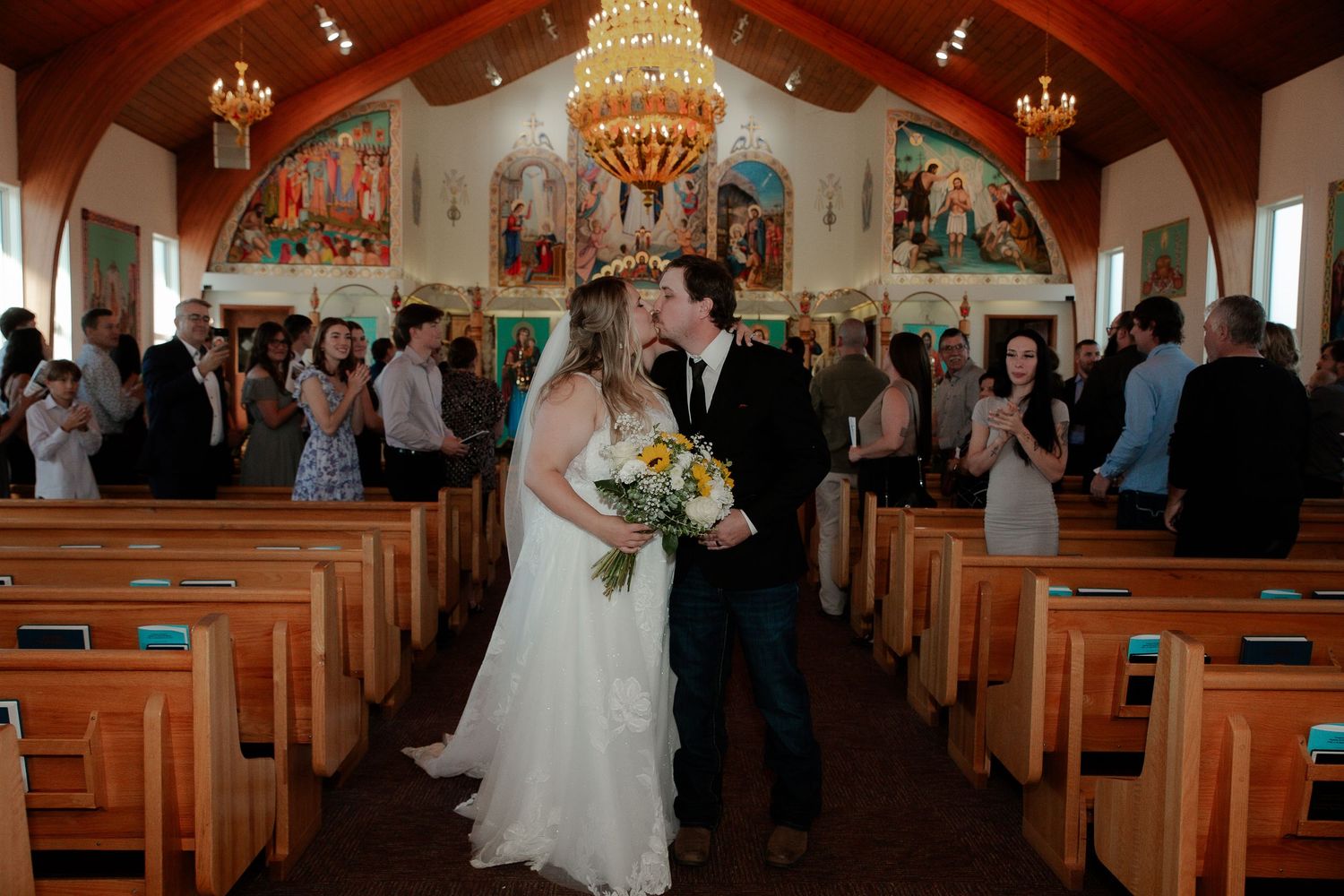 A church wedding ceremony with elegant chandeliers and wooden pews filled with guests in Saskatoon, Saskatchewan.