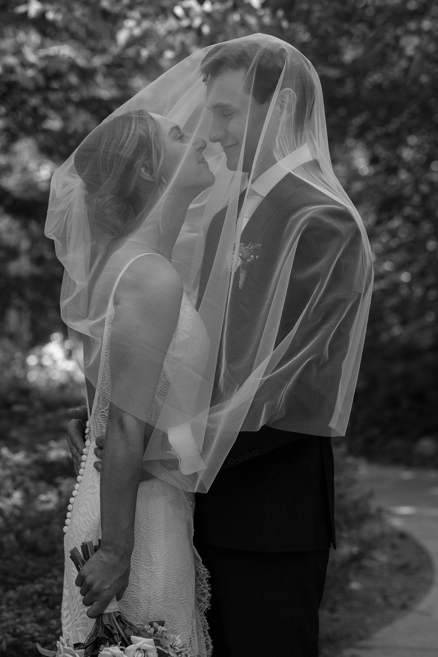 Intimate black and white portrait of a couple embracing under a flowing wedding veil at Boffin's Gardens in Saskatoon.