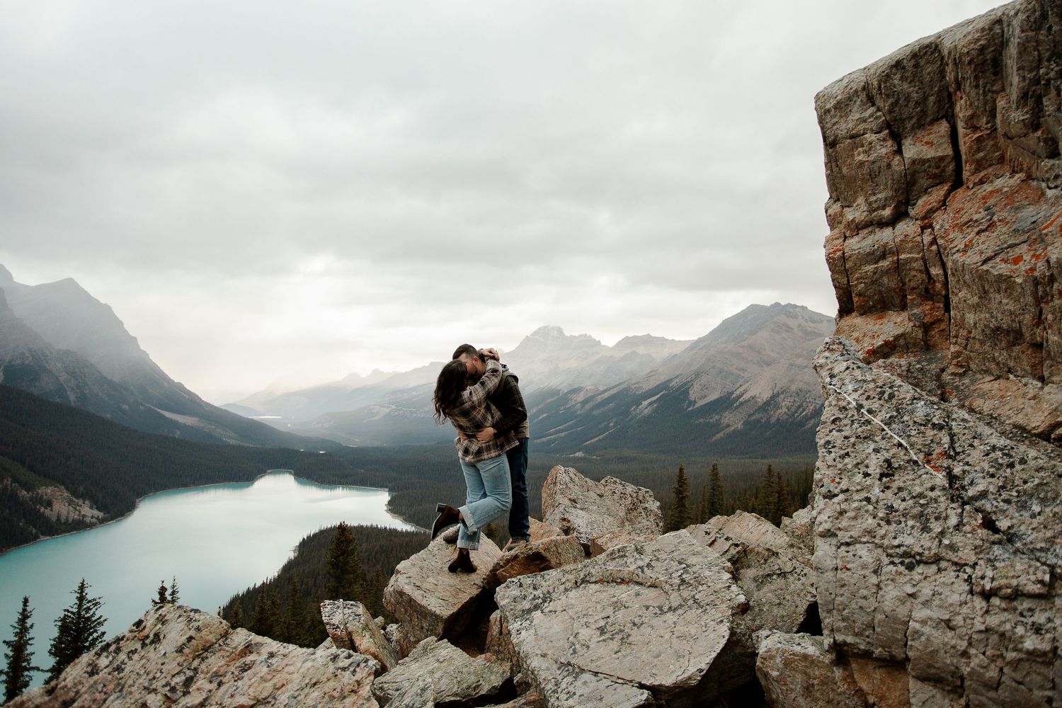 Couple embracing on rocky mountain overlook with stunning turquoise lake and misty peaks in Banff National Park.