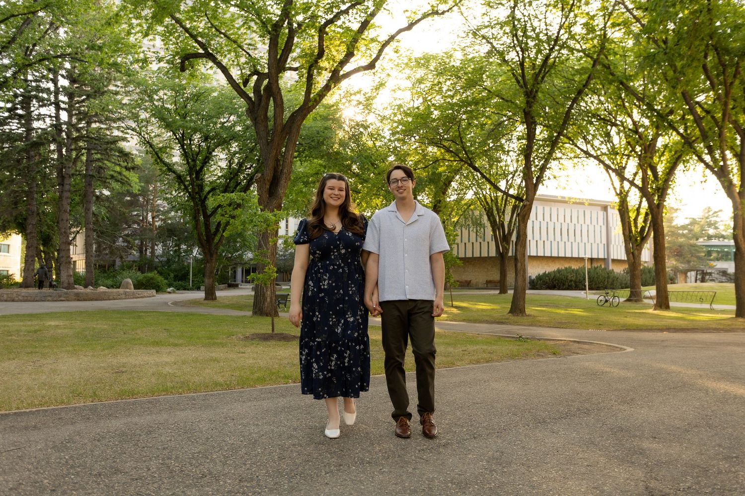 Couple walking hand-in-hand on a tree-lined campus path during golden hour sunset.