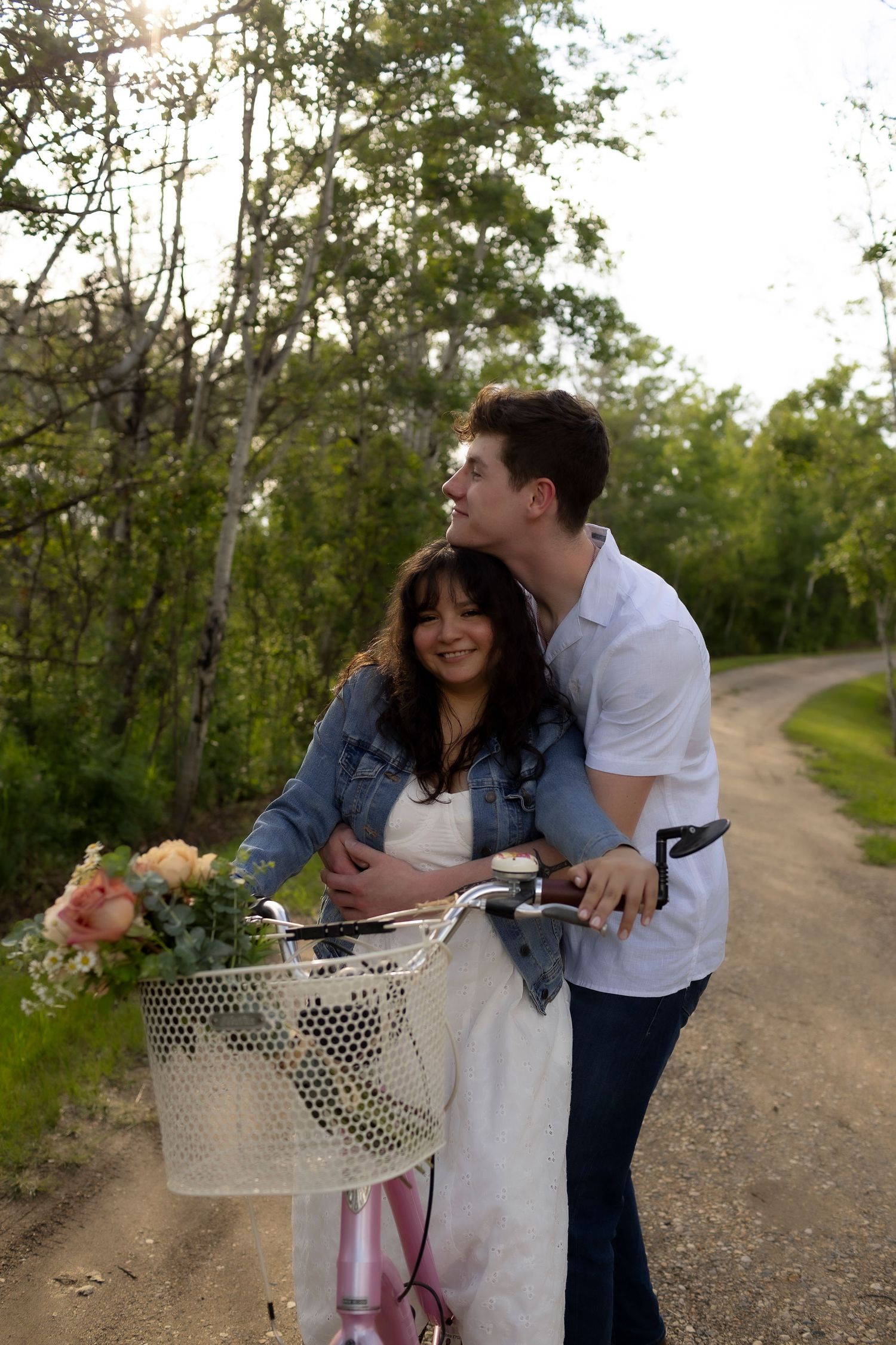 A young couple shares a romantic moment on a country road with a vintage pink bicycle adorned with a flower basket.