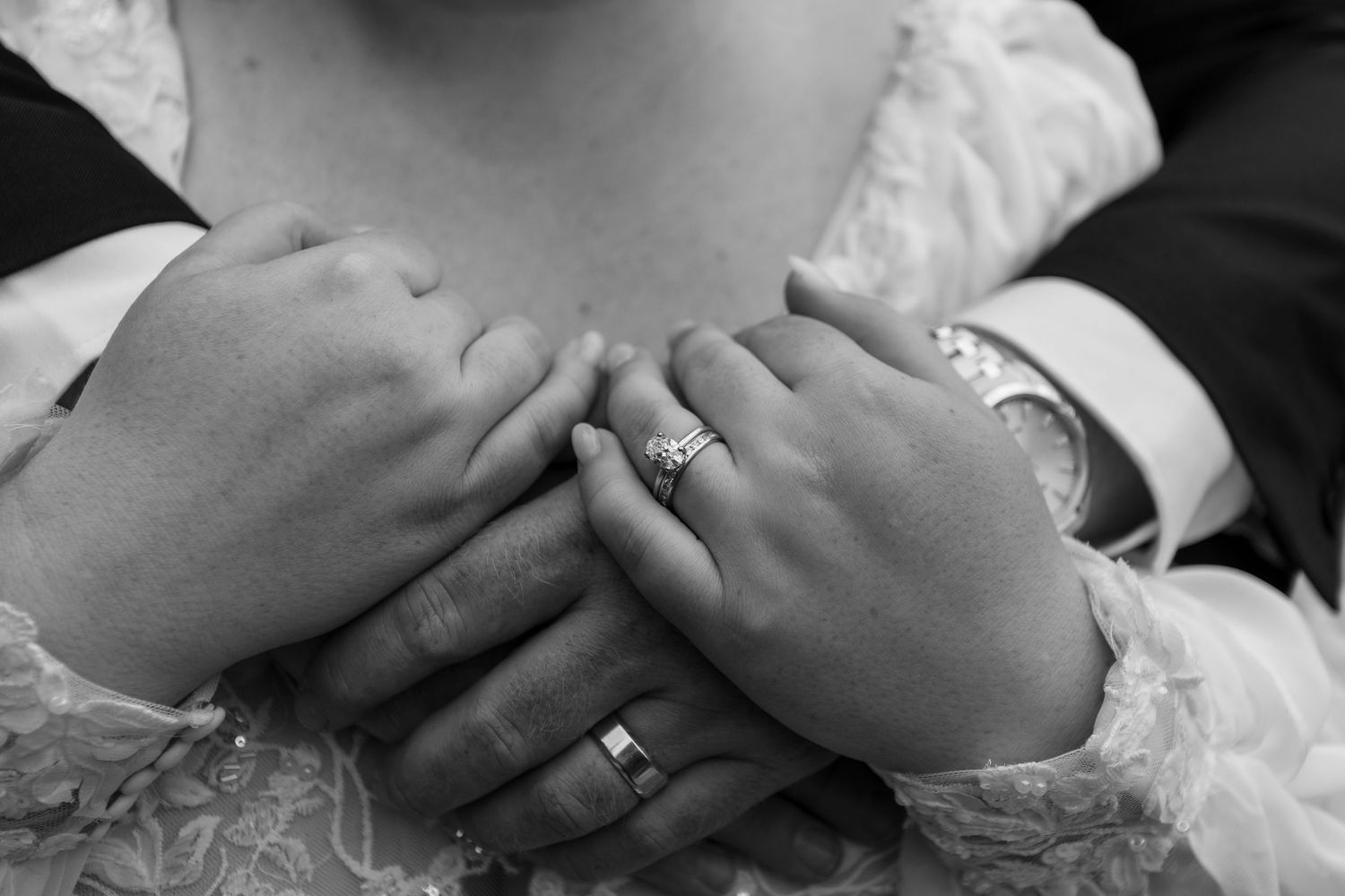 Black and white photo of bride and groom holding hands, showing wedding rings and engagement ring.