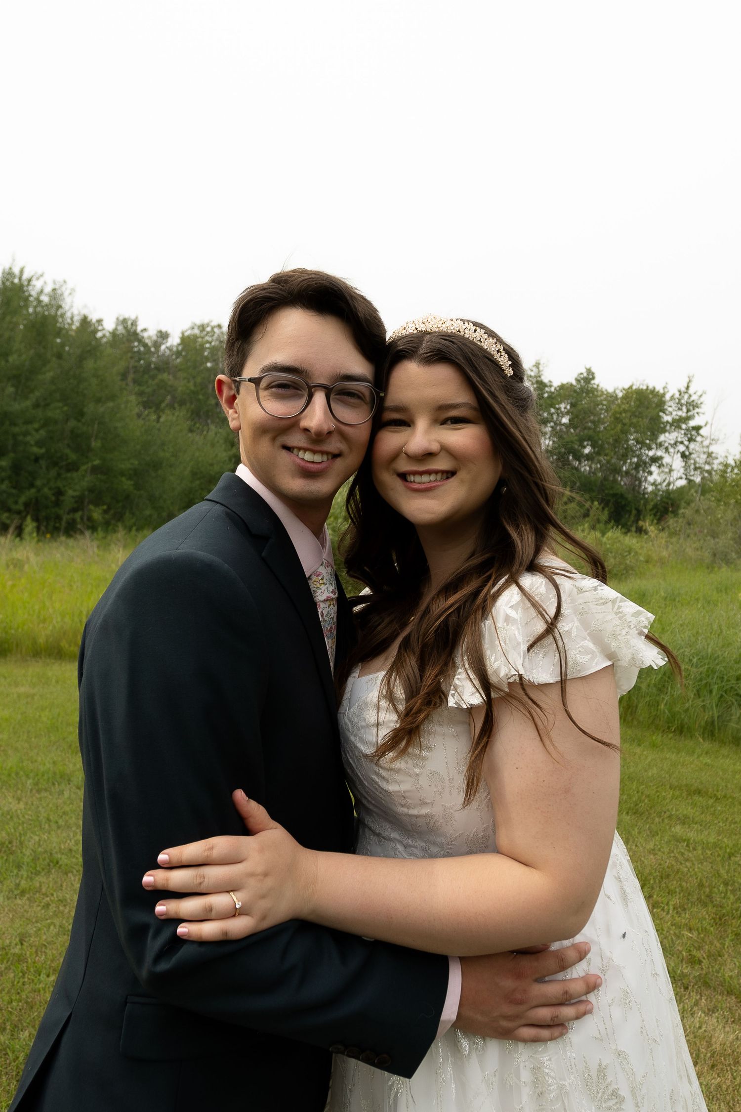 A couple embraces outdoors in wedding attire with a natural green background.