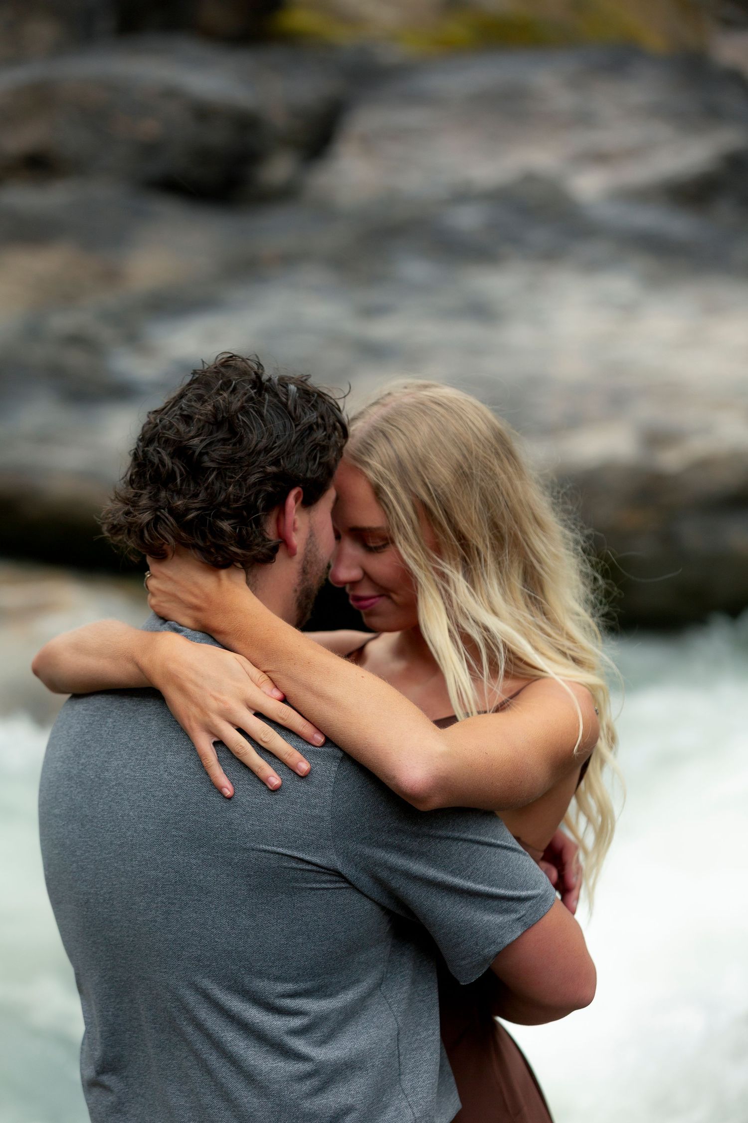 A couple shares an intimate embrace against a backdrop of rushing water and rocks Takakkaw Falls in British Colombia.