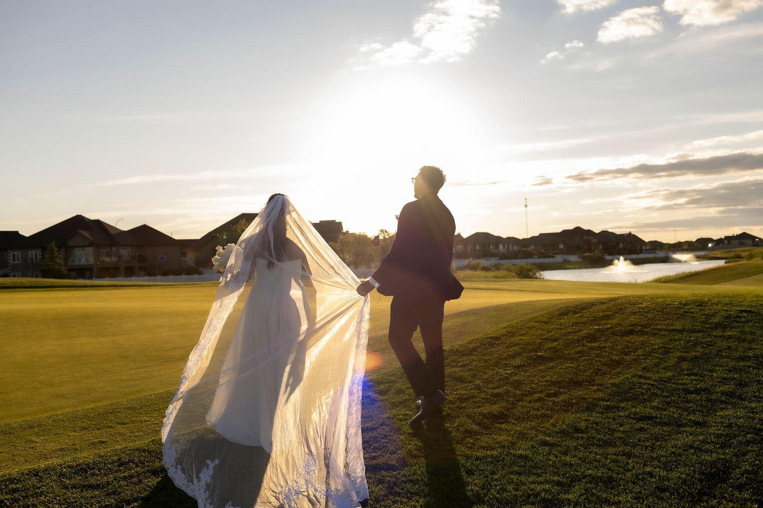 A couple walks hand in hand across a golf course during golden hour sunset.
