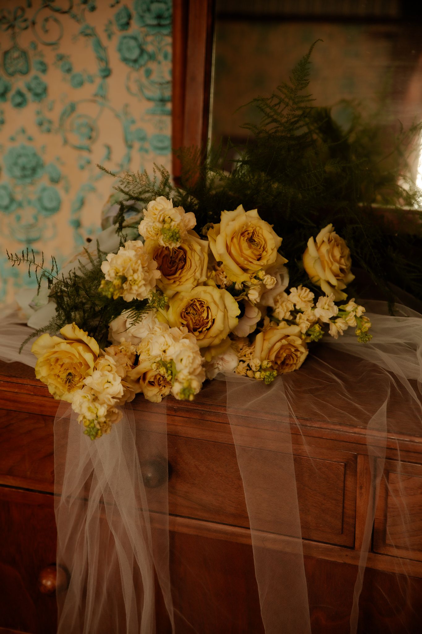 Cream and white floral arrangements with tulle decorating a wooden mantel.