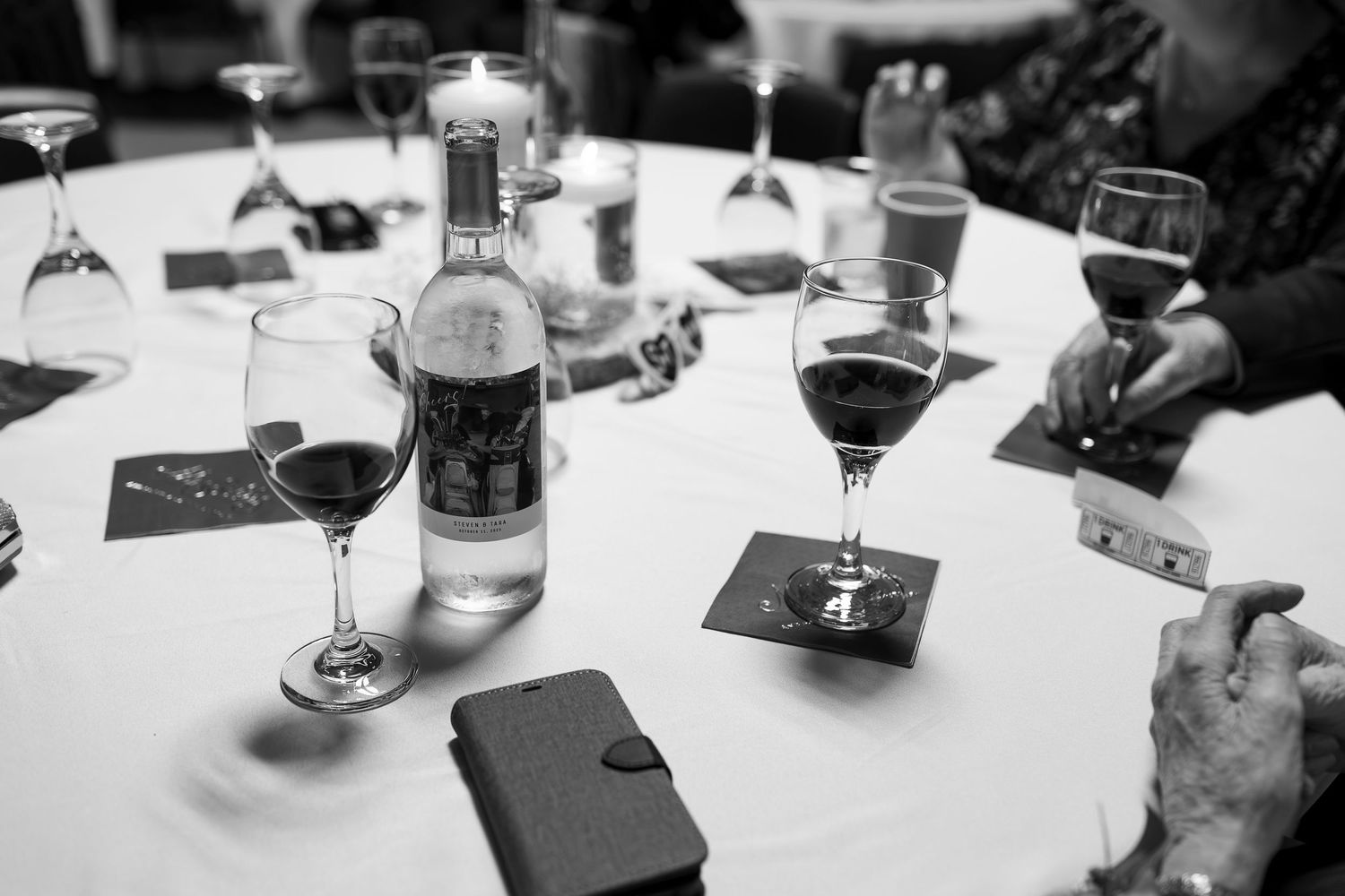 Black and white photo of wine glasses and water bottle on white tablecloth at elegant dinner event.