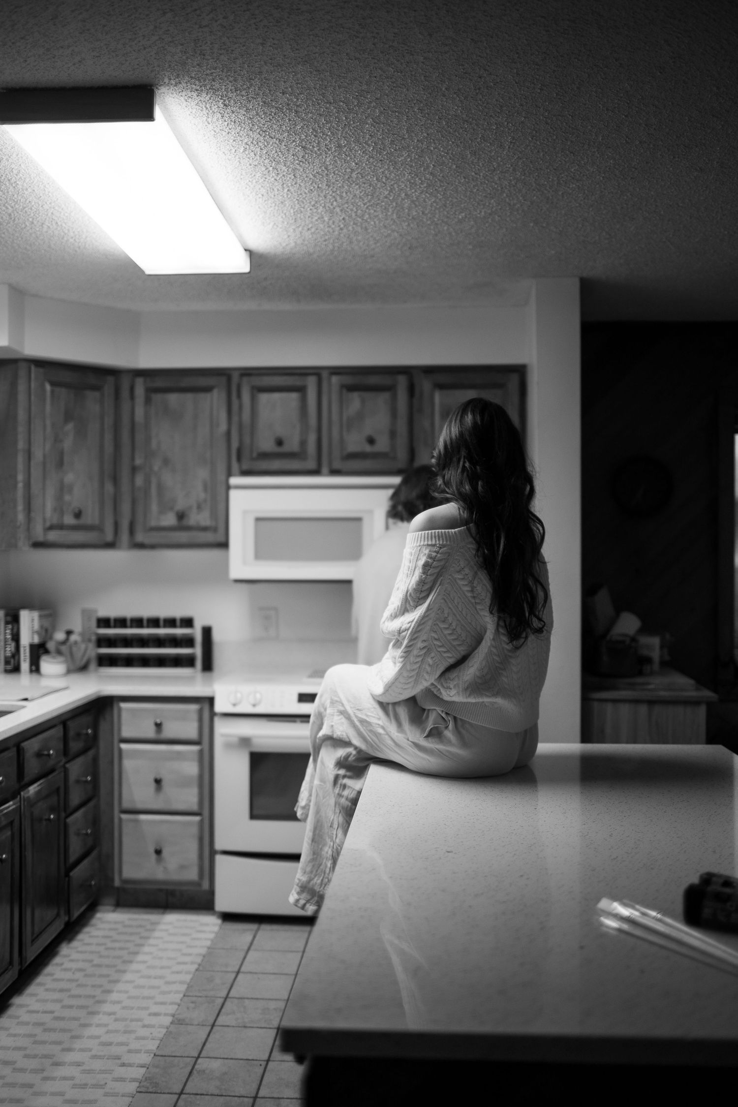 Black and white photo of a woman sitting on a kitchen counter, gazing away in a cozy sweater.