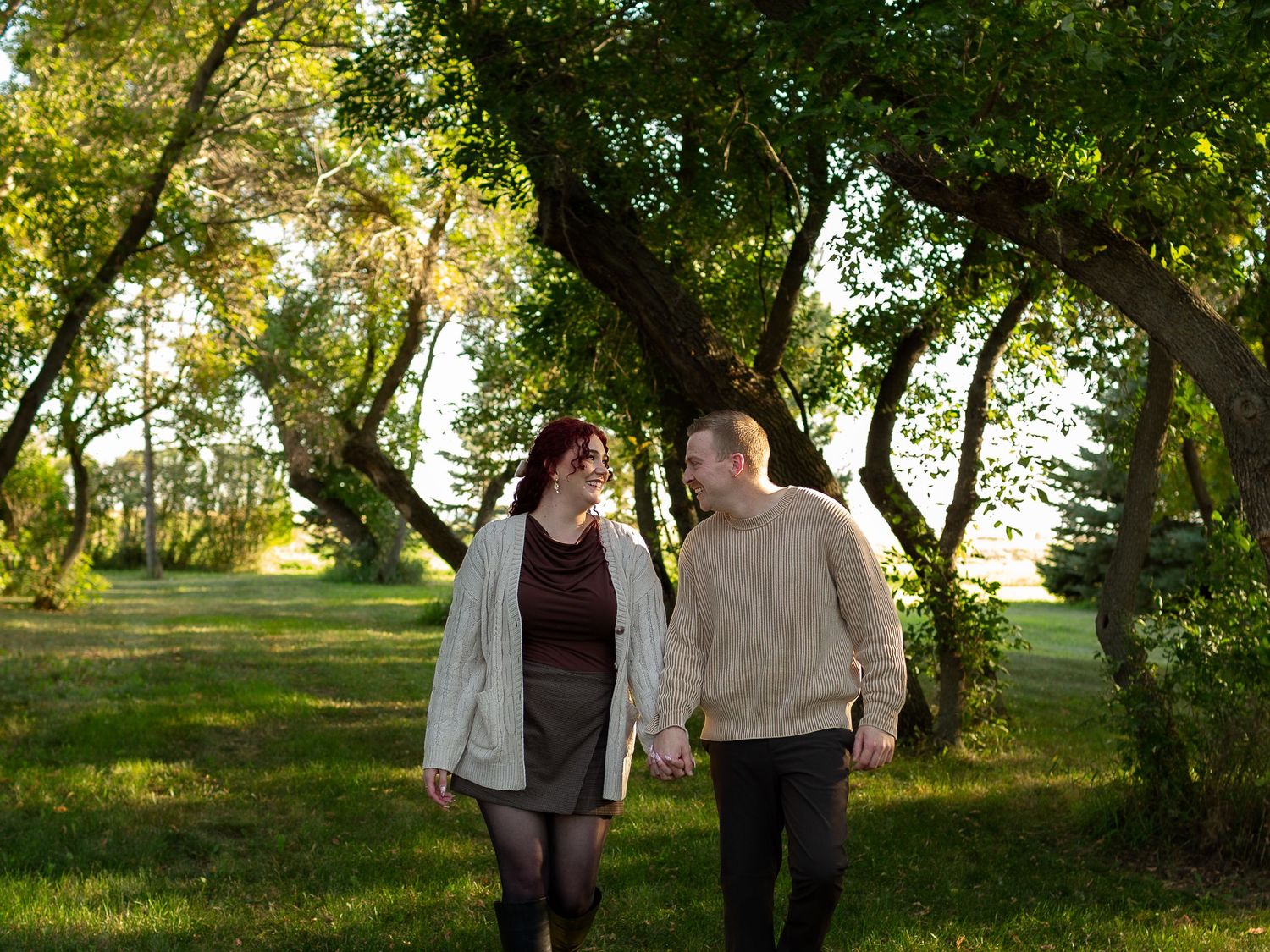 Couple walking together on a tree-lined path during golden hour.