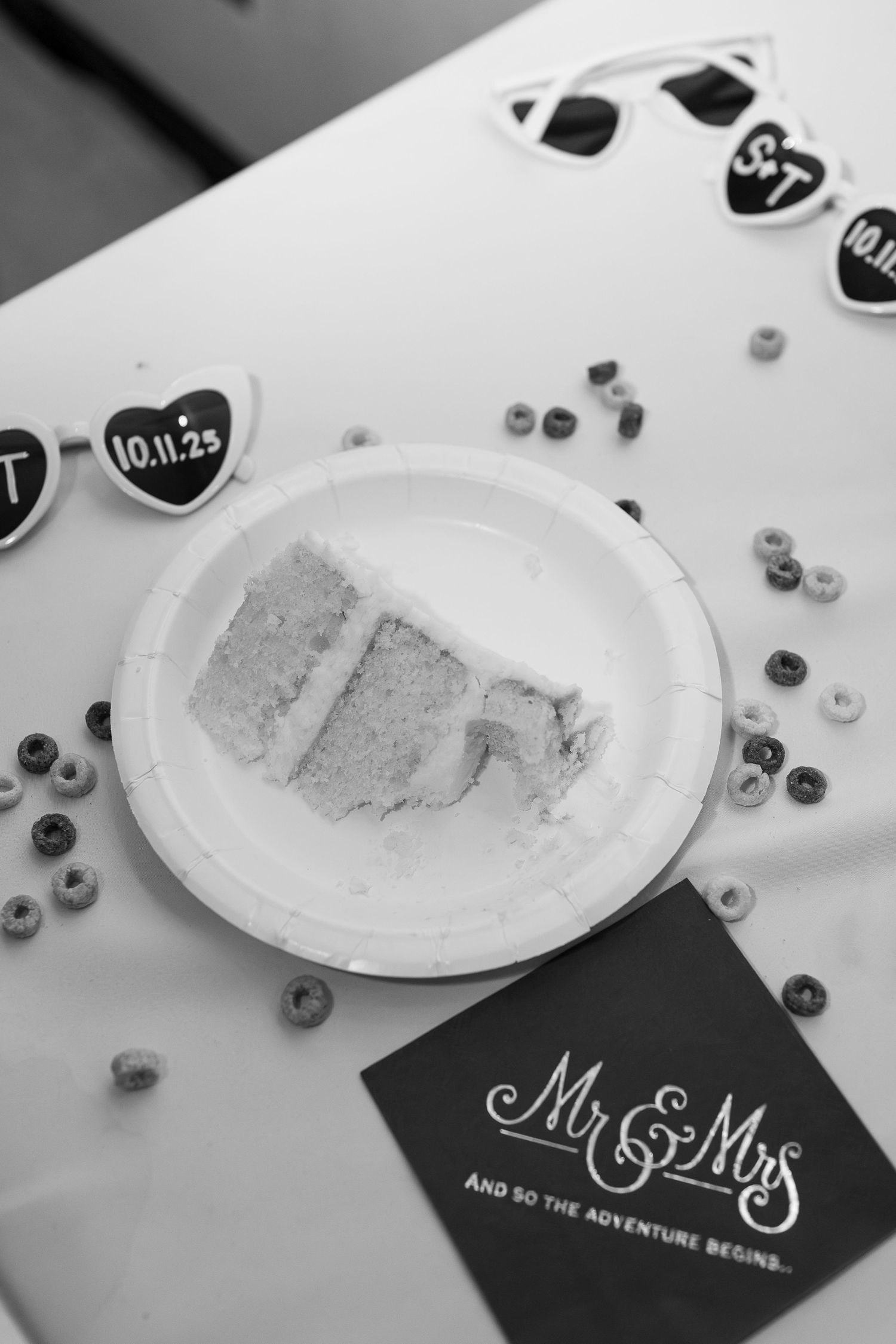 Black and white wedding photo of cake slice on paper plate with Mr & Mrs napkin and heart decorations dated 10.11.25.
