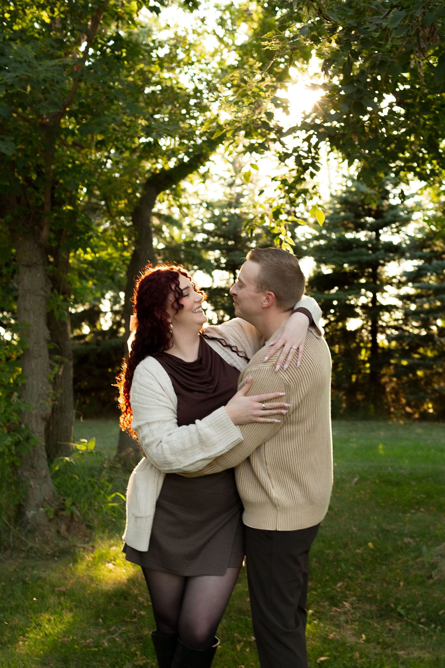 A romantic autumn sunset portrait of a couple embracing under trees with golden light filtering through the leaves.