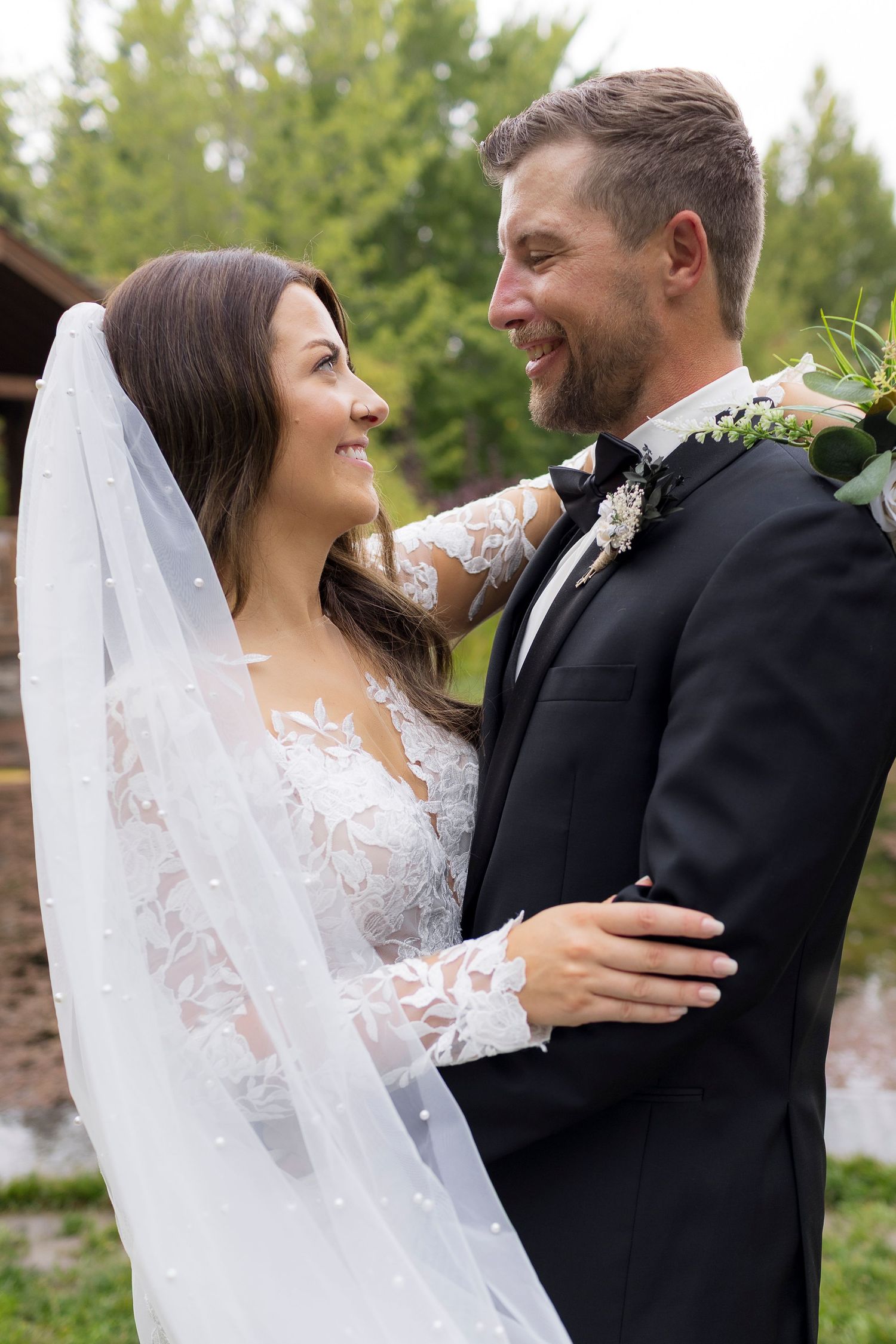A tender wedding moment captured outdoors with the bride in lace and veil embracing her groom.