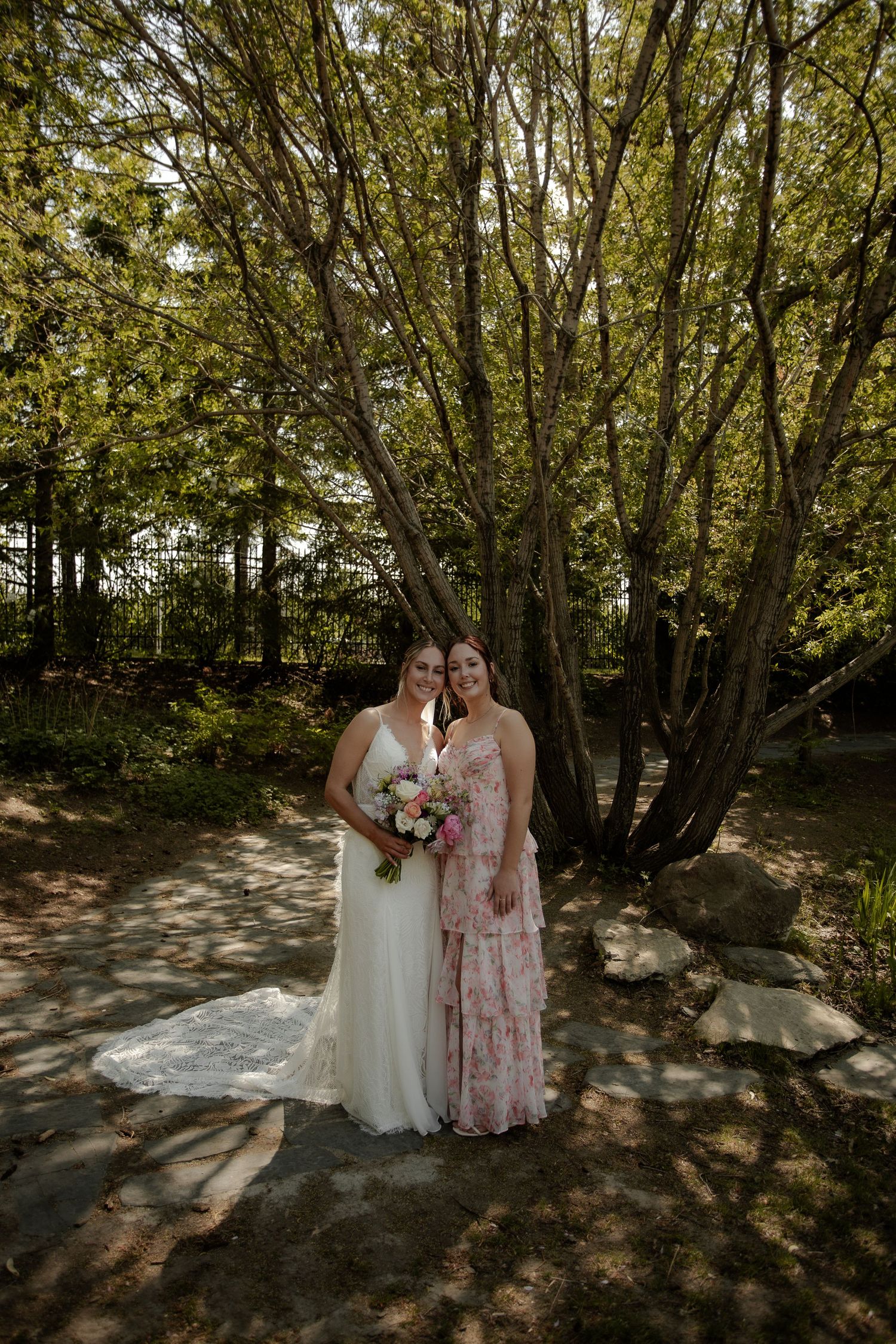 A couple in wedding attire shares an intimate moment in a wooded forest setting with dappled sunlight.