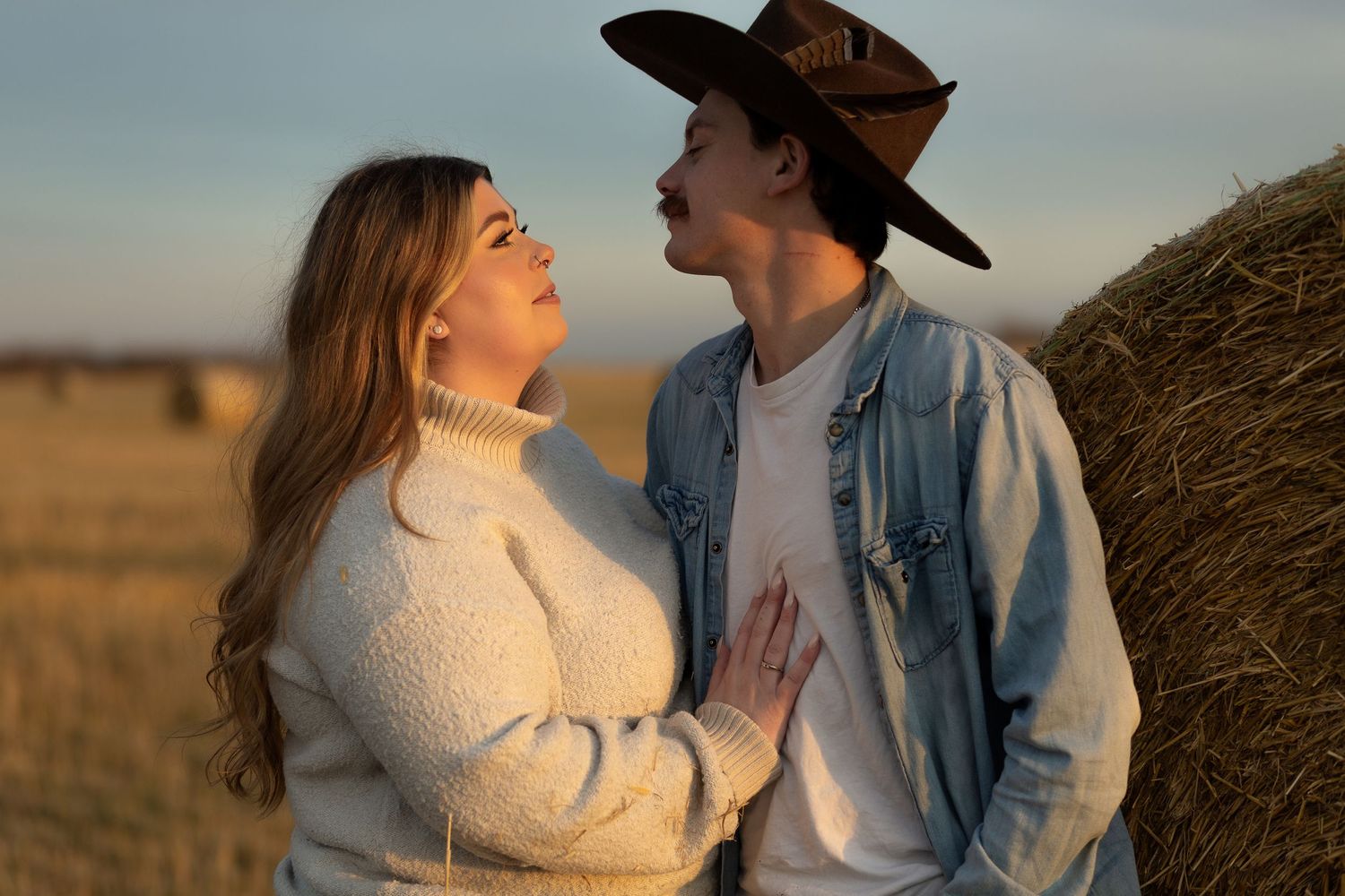 Romantic sunset portrait in a field with hay bales and warm lighting.